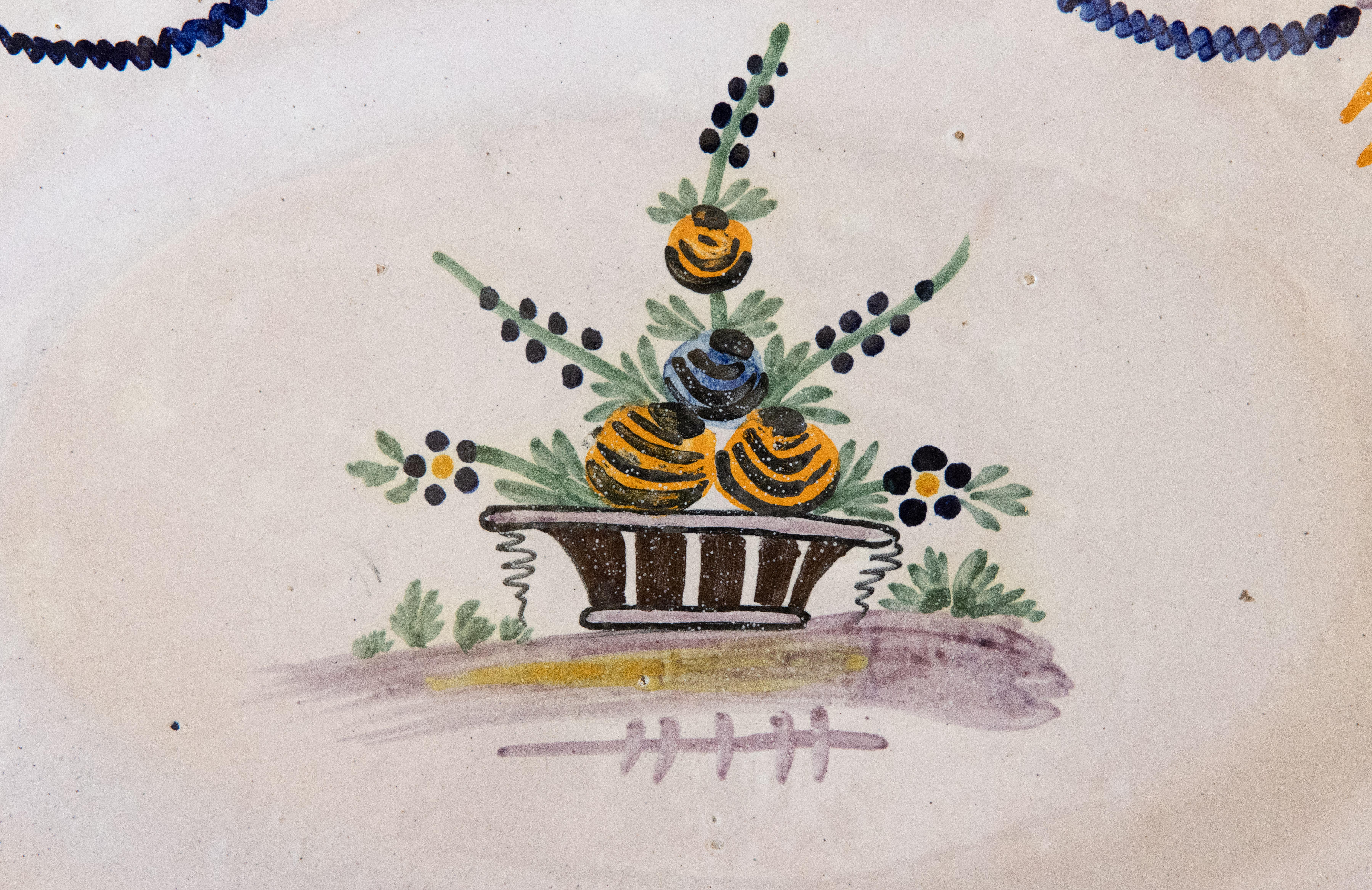 Magnifique plateau mural ovale en faïence peint à la main par les Moustiers au 19e siècle. Ce rare plat décoratif présente des détails remarquables avec un pot de fleurs peint à la main au centre, entouré d'une guirlande festive et d'un ravissant