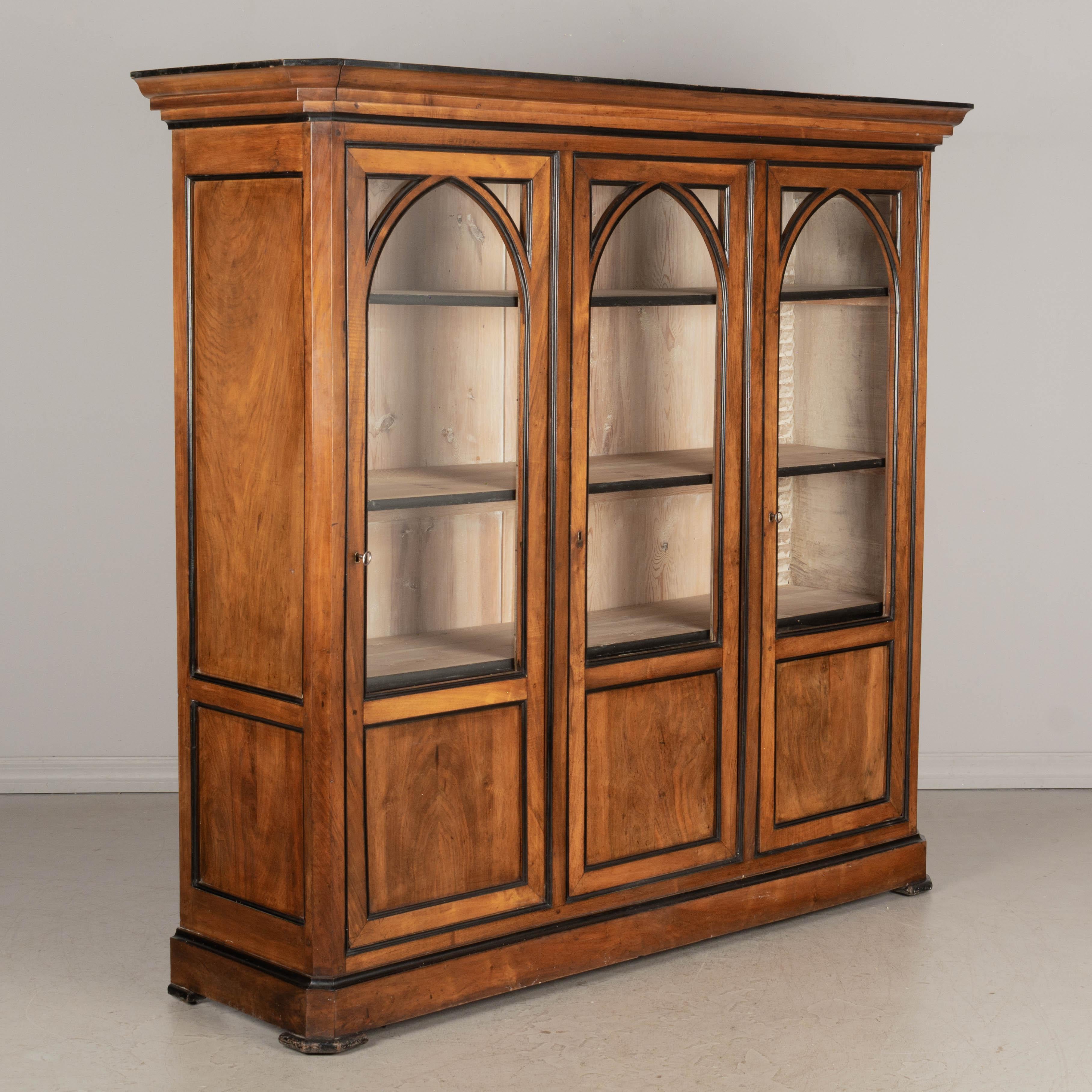 A pair of 19th century French Napoleon III bibliotheques, or bookcases made of solid walnut with ebonized trim and paned glass doors. Interior is unfinished and has three adjustable shelves with black trimmed edge. Locks in working order with four