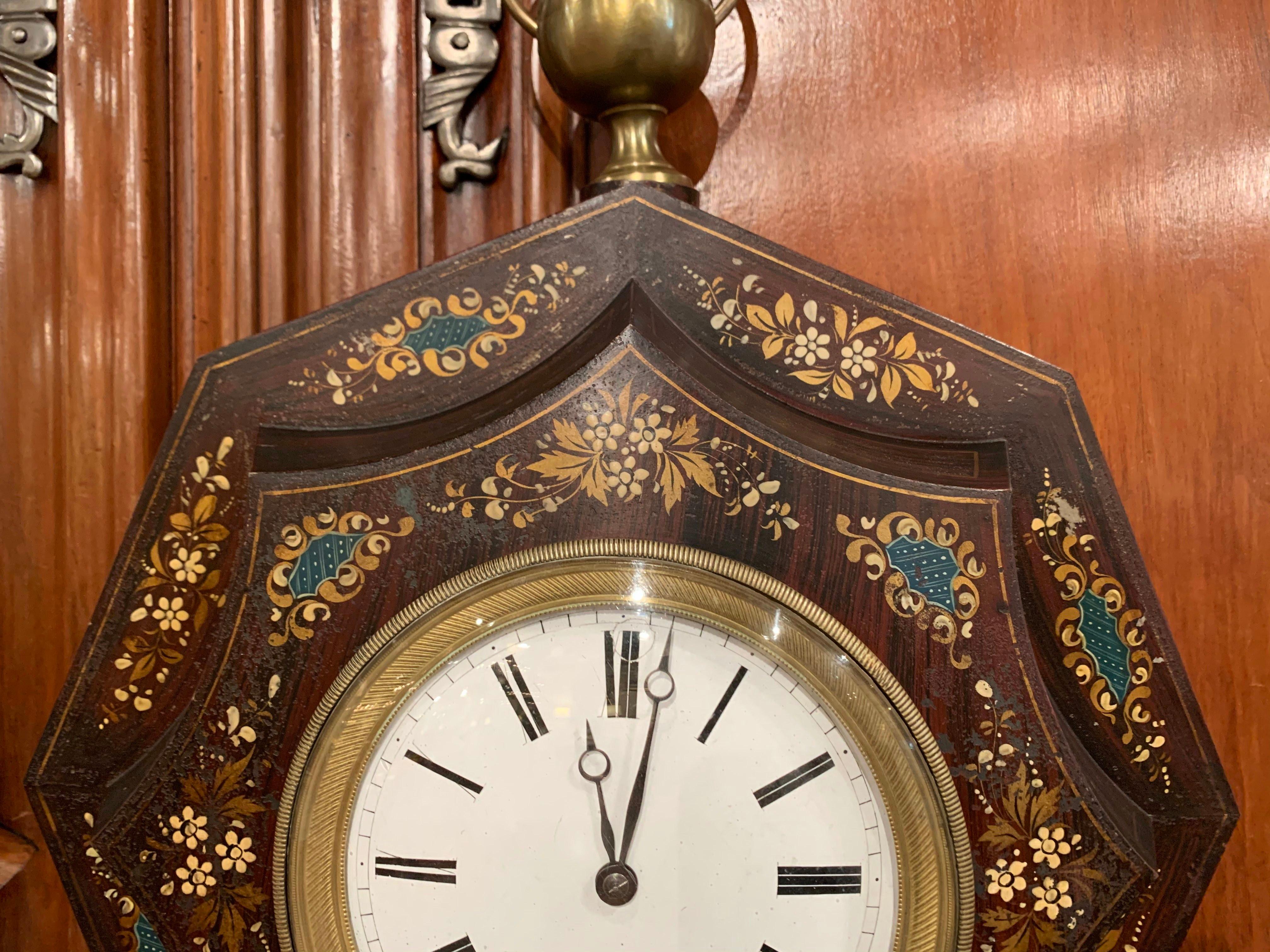 This feminine wall clock was created in France, circa 1870. Octagonal in shape, the antique tole time keeper features a decorative round brass finial at the top and embellished with a brass rim around the front door; the clock has a rich, black
