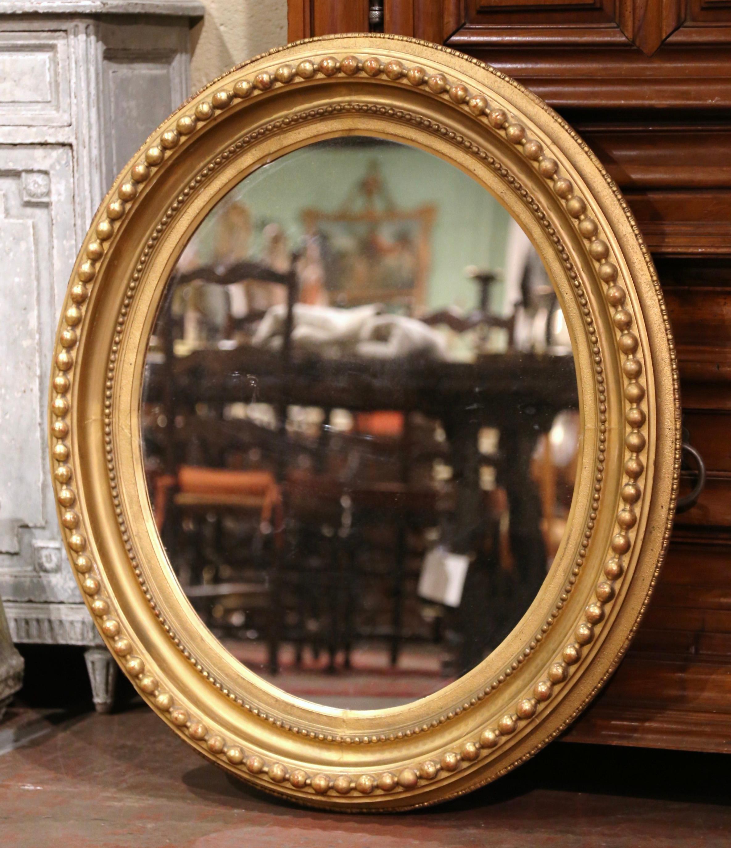 Decorate a powder room or entryway with this elegant antique wall mirror. Crafted in France, circa 1950, the oval frame is decorated with bead motifs in high relief around the frame. The large mirror, dressed with mercury glass, is in excellent