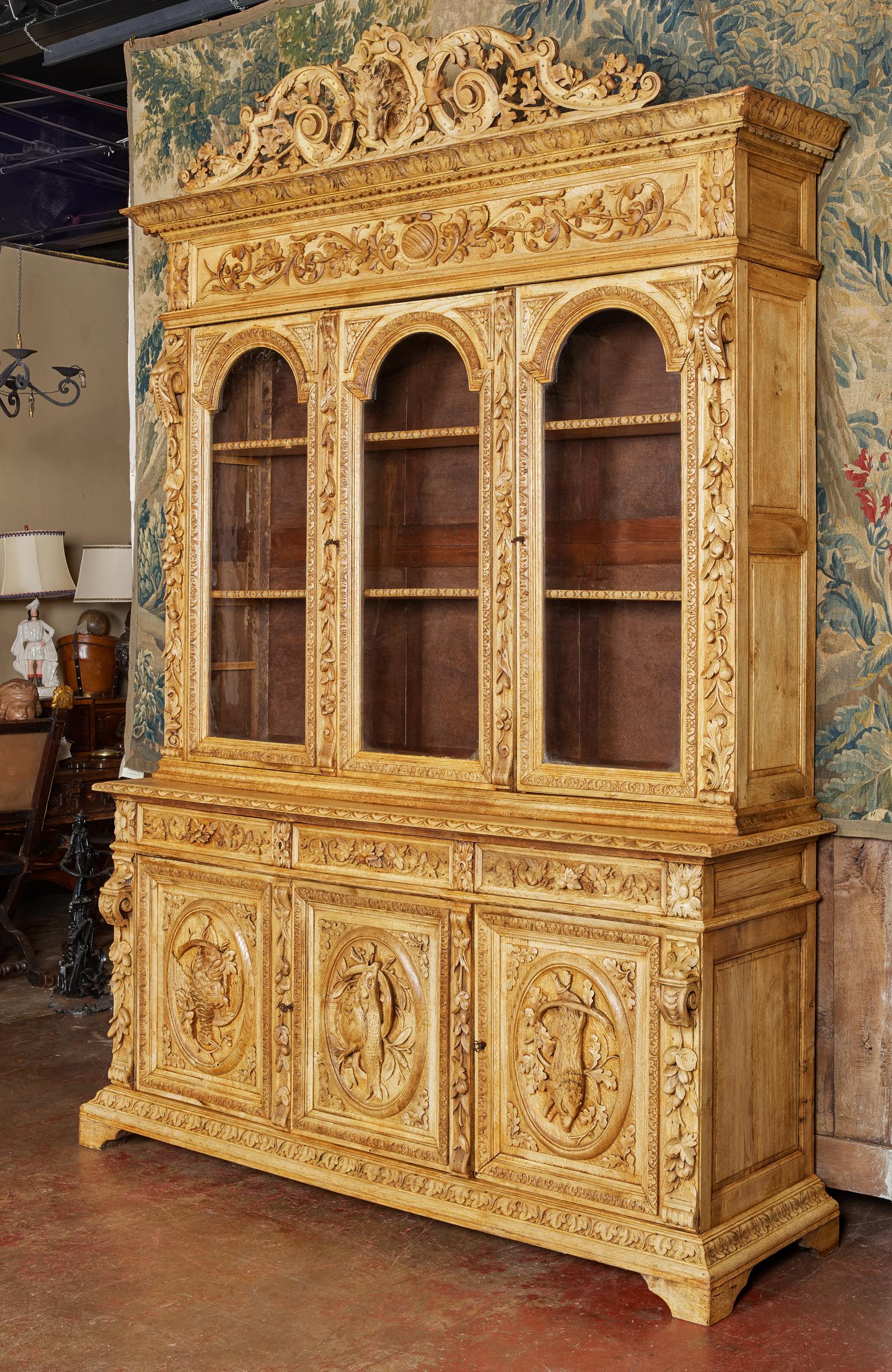 This spectacular antique hunt cabinet was crafted in northern France circa 1870. The large bookcase built in two sections, stands on a molded base further raised on bracket feet, and features exquisite carvings starting at the pediment with a