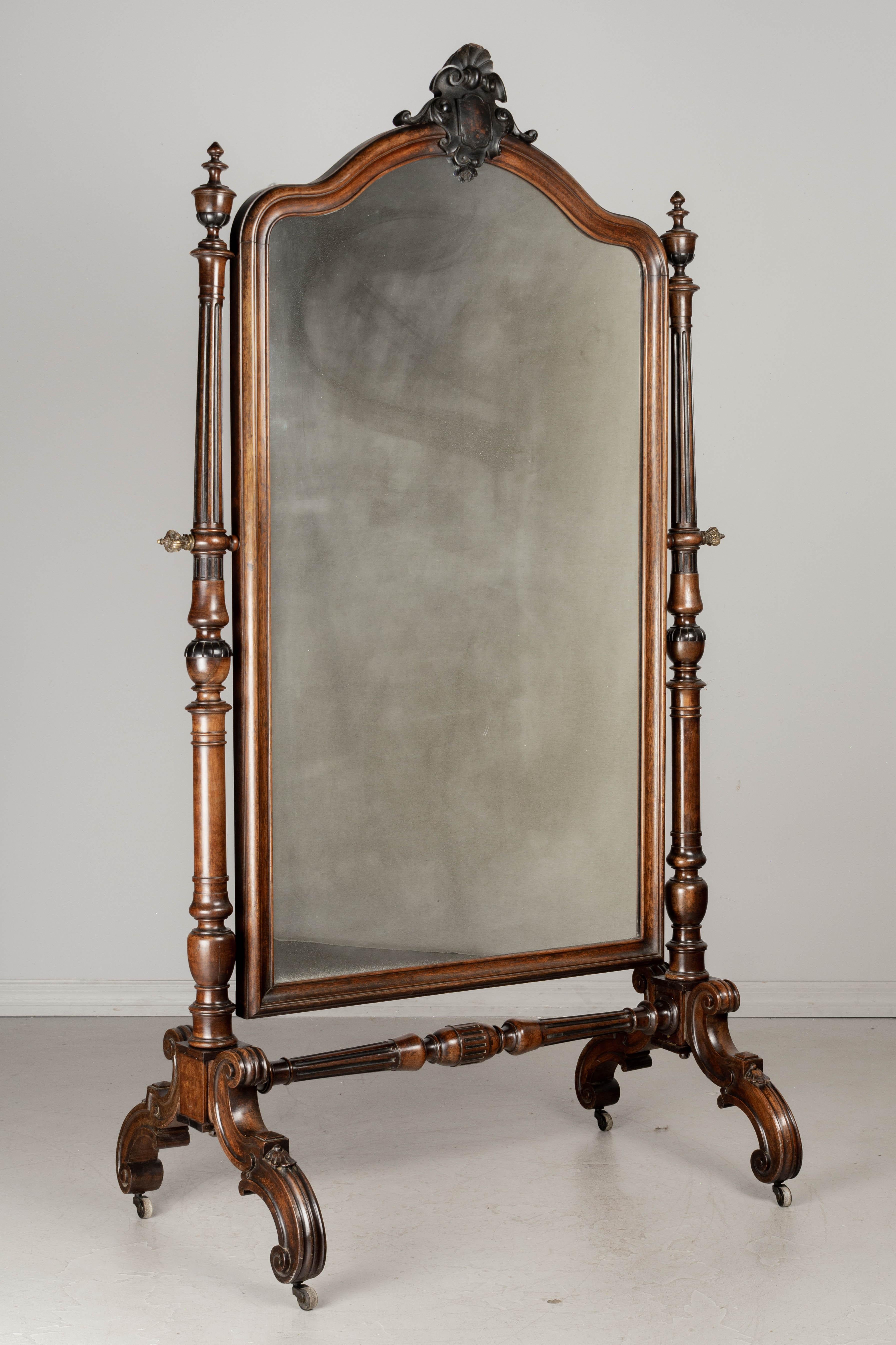 A large 19th century French Napoleon III chevalet, or cheval mirror, made of rosewood with ebonized details. Turned columns and finials and nicely carved details on the scroll form legs and shell form crest at the top. Cast brass knobs and original