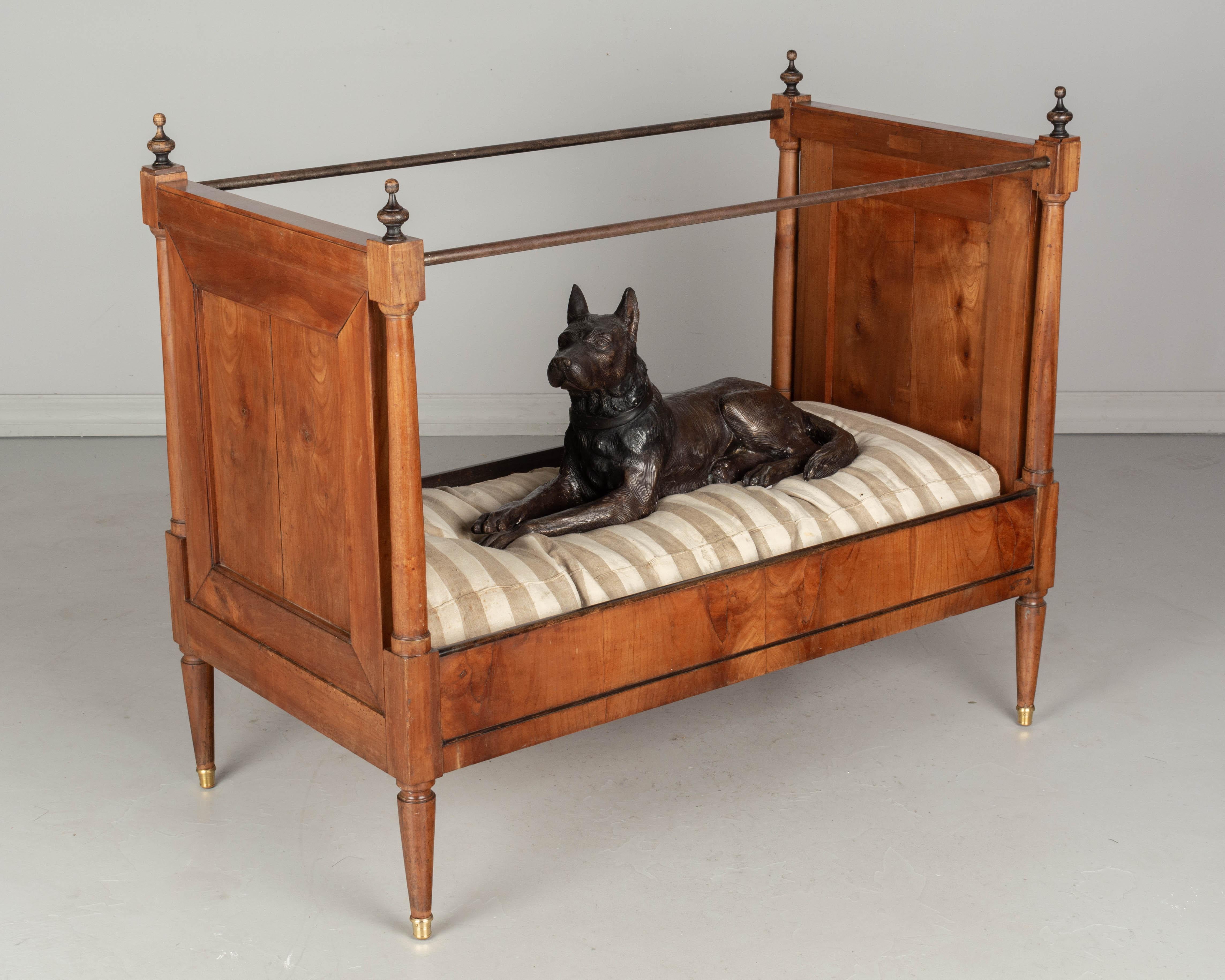 A 19th century French Napoleon III Period child's bed made of solid cherry wood, with column form supports and iron curtain rails. Beautiful book matched wood panels and side rails with ebonized trim. Old mattress upholstered in striped ticking