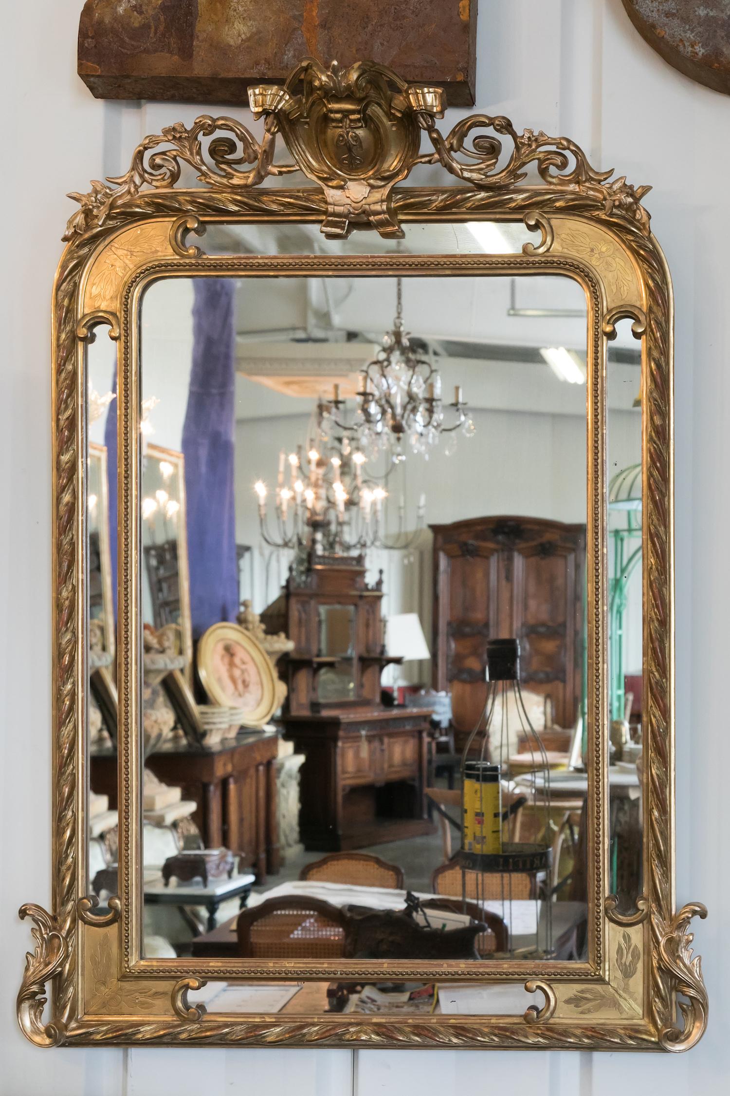French Napoleon III period pareclose mirror with elaborately carved giltwood frame with red oxidation showing through. Decoration includes a central crest carved in high relief flanked by curving acanthus leaves and flowering branches with the inner