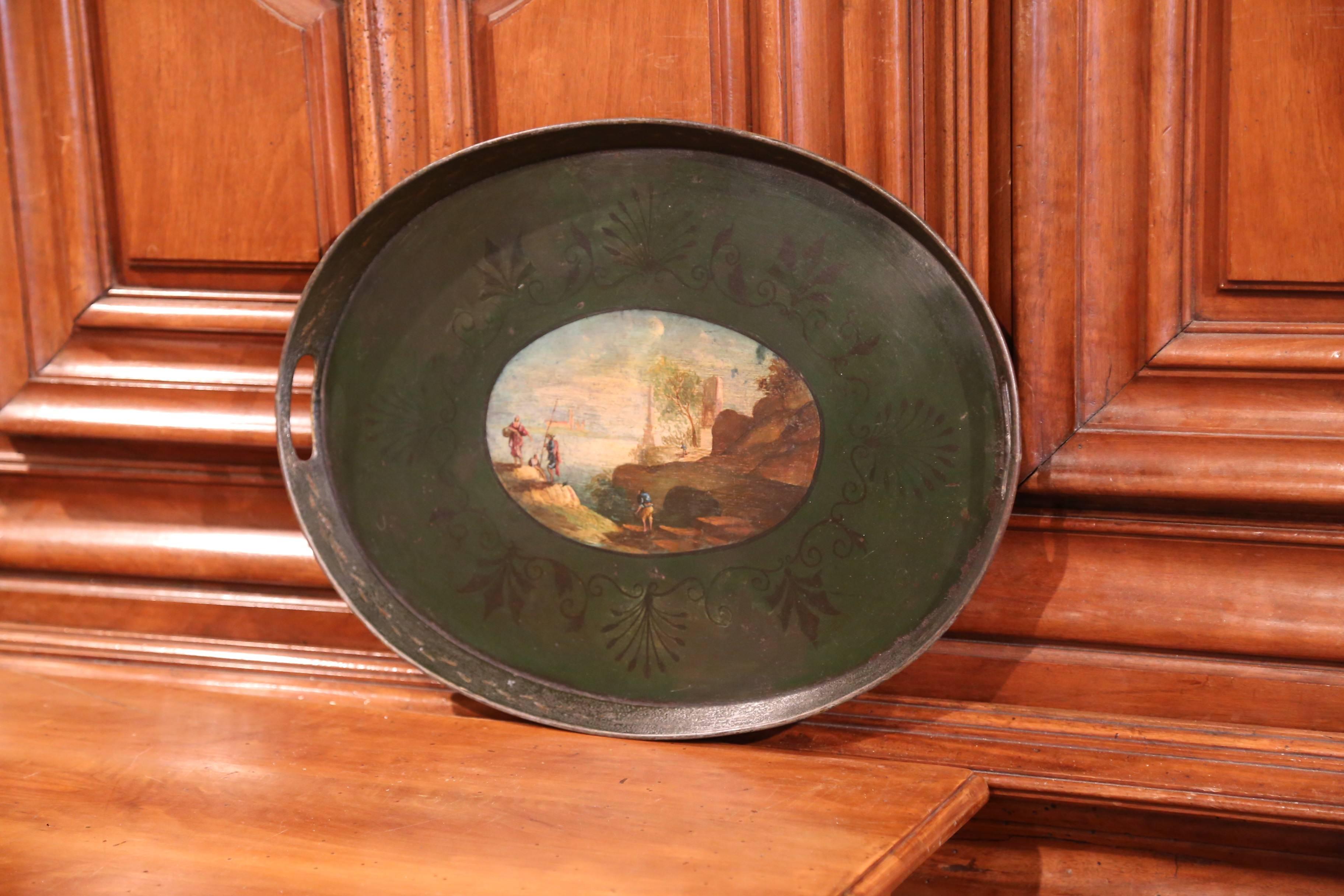This elegant antique oval tole tray was crafted in France, circa 1870, the colorful platter with side handles, features an oval center medallion with coastline scene, cliffs, trees, fishermen and buildings in the background. The tray table is in