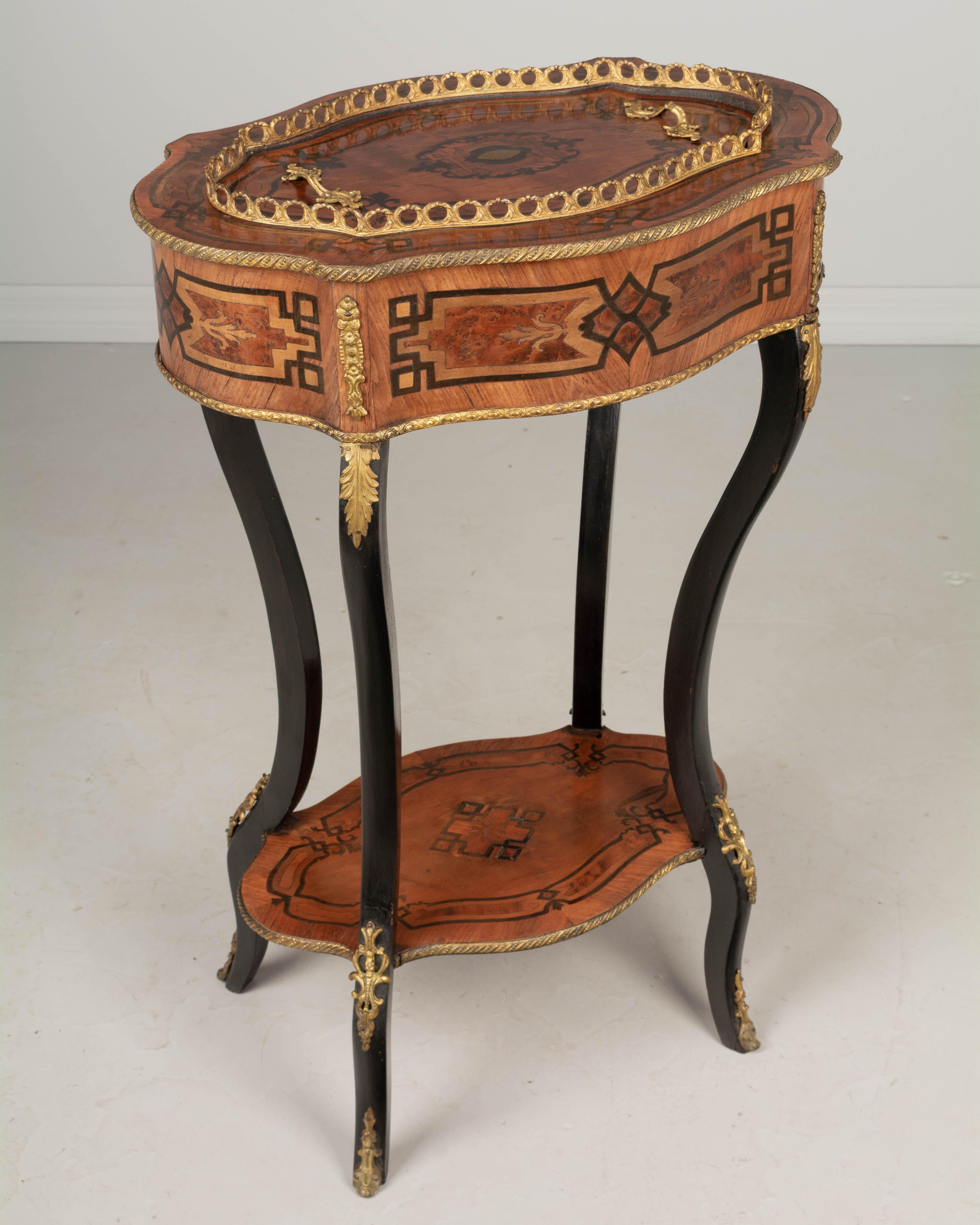 A 19th century French Napoleon III bronze mounted marquetry jardinière, or plant stand with inlaid veneers of mahogany and walnut. Curved ebonized legs joined by a lower shelf. The shaped oval top has cast bronze handles and lifts off to reveal and