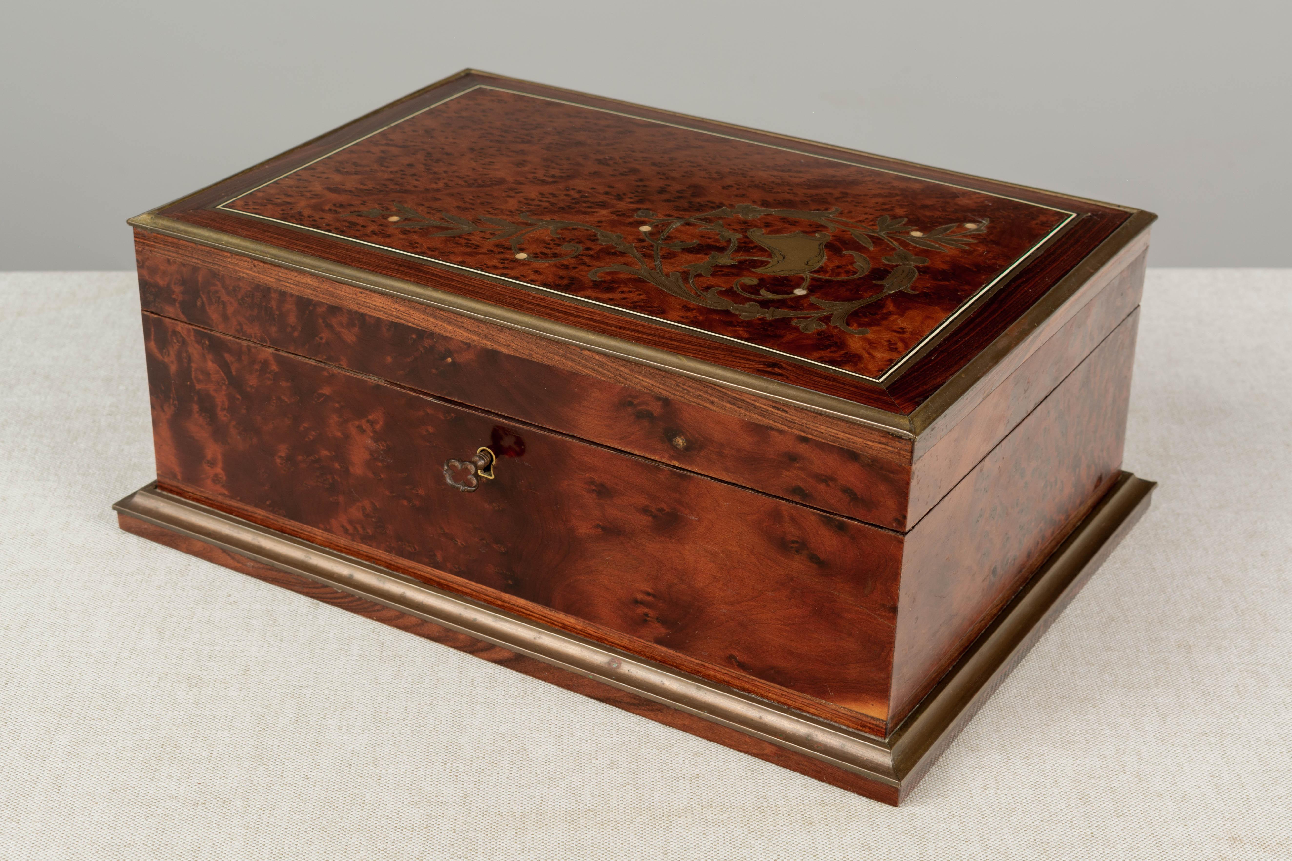A 19th Century French Napoleon III marquetry sewing box. Made of mahogany with thuya wood top inlaid with brass and mother of pearl. Brass trim frames the lid and the base. The interior is lined in red silk and is fitted with a collection of 15