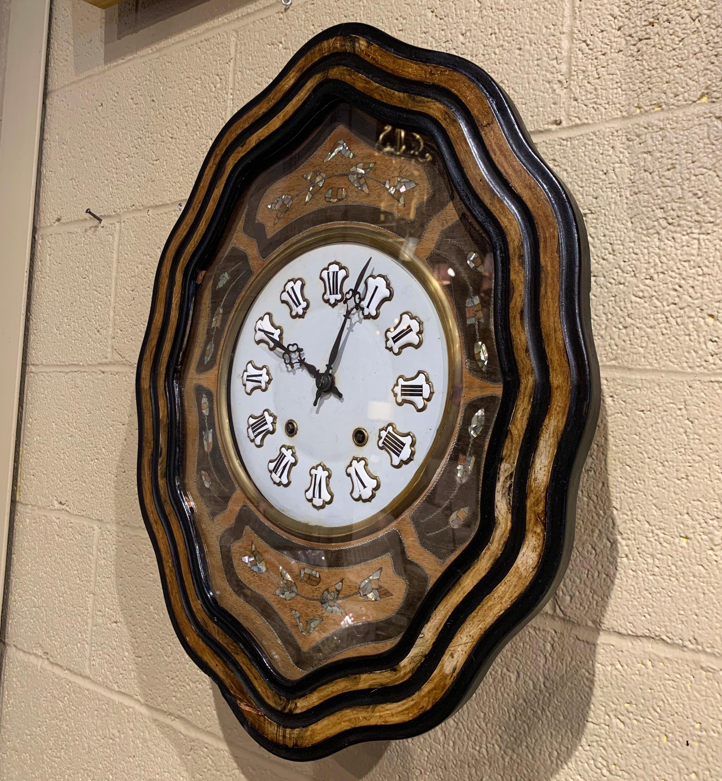 This colorful antique wall hanging clock was crafted in France circa 1870; oval in shape, the time keeper has a two-tone black and wood painted around the perimeter, the time keeper features colorful handcrafted mother of pearl floral and foliage