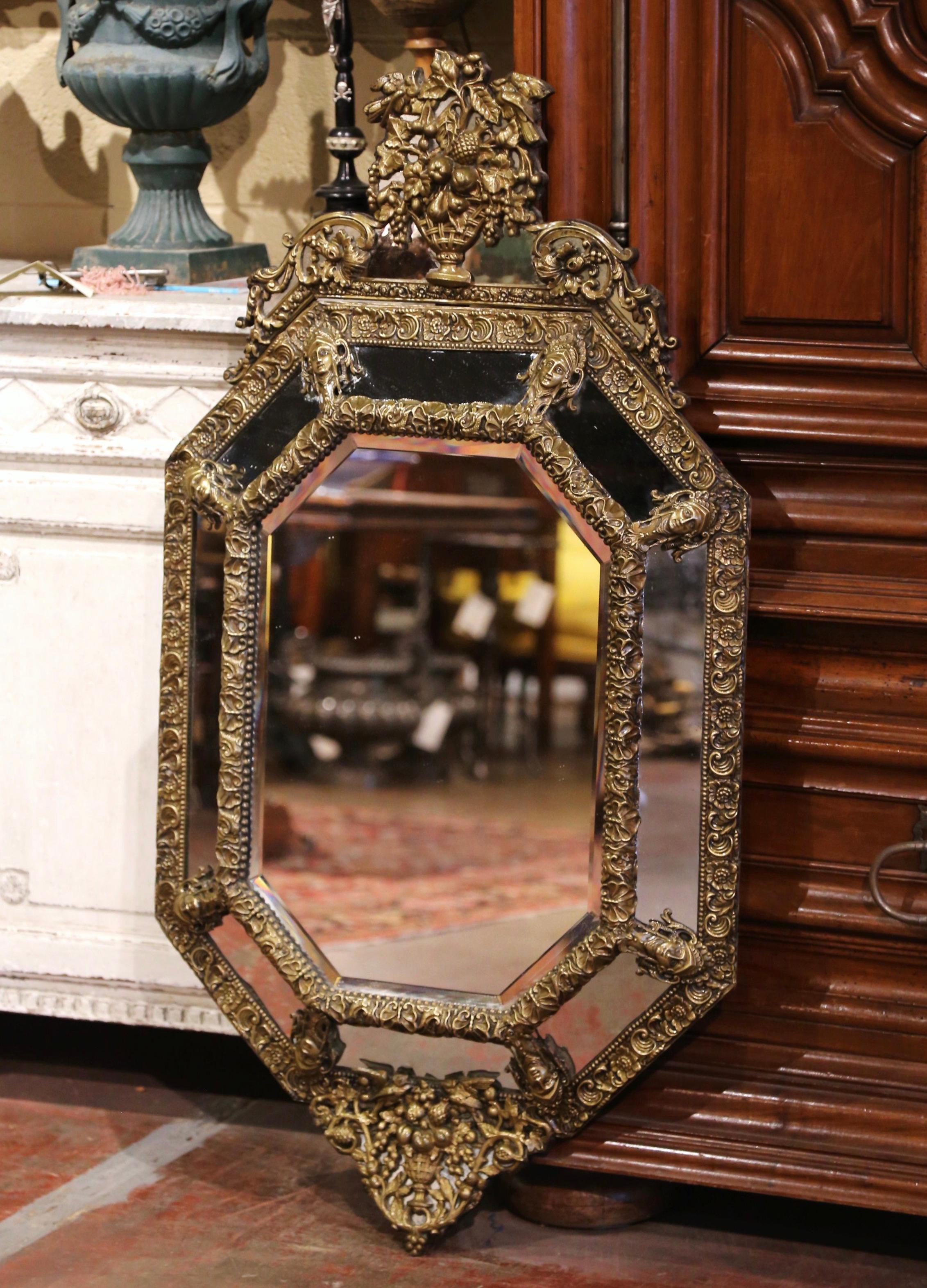 Created in France, circa 1870, the elegant antique wall mirror is octagonal in shape and decorated with intricate repousse decor around the frame; it includes a large vase cartouche at the pediment filled up with different fruit and flanked with