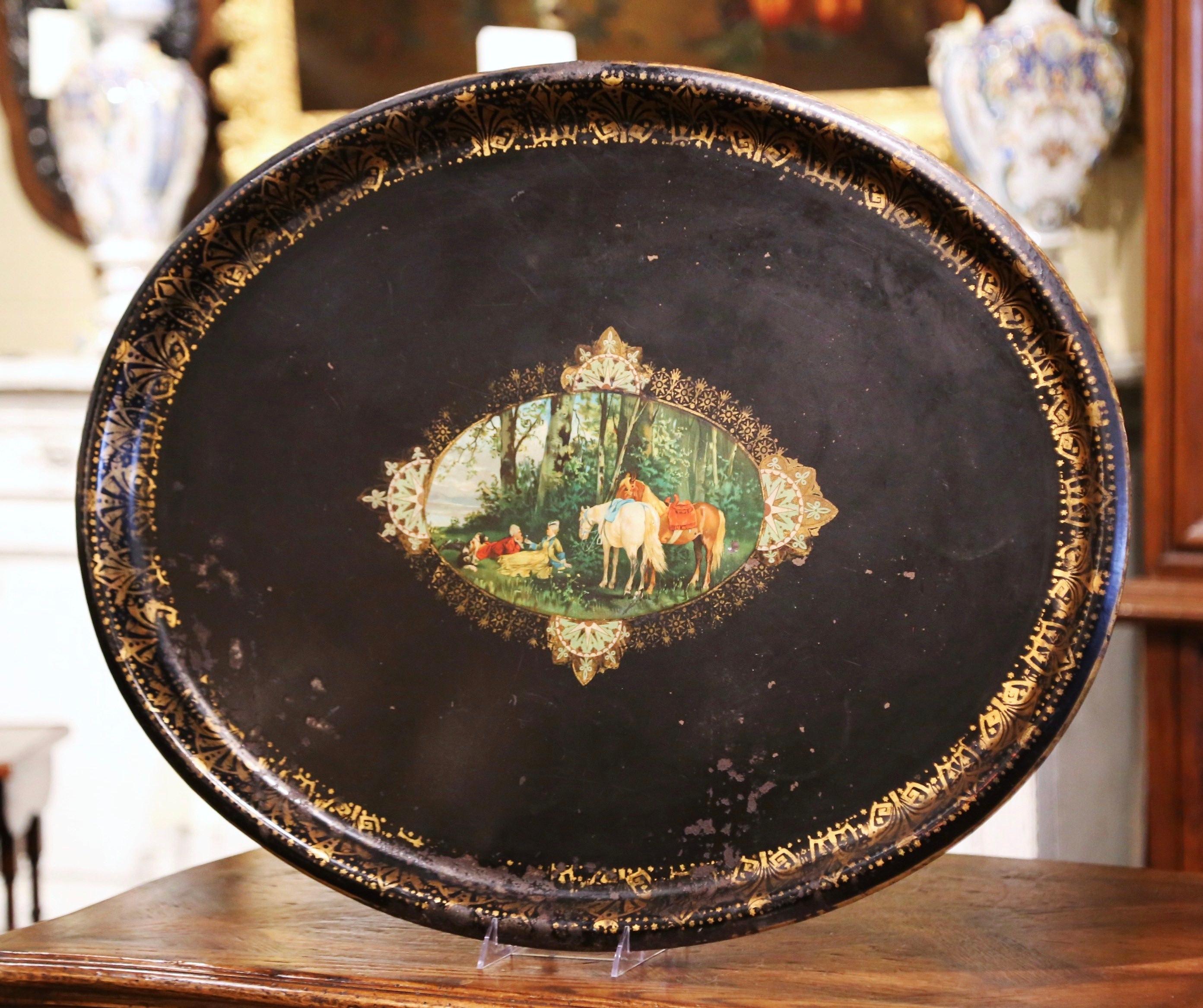 This elegant antique tray was created in France, circa 1870. Oval in shape, the large black tole platter is embellished by hand painted gilt decor around the lip, and a colorful hand painted center medallion depicting a romantic picnic in the park