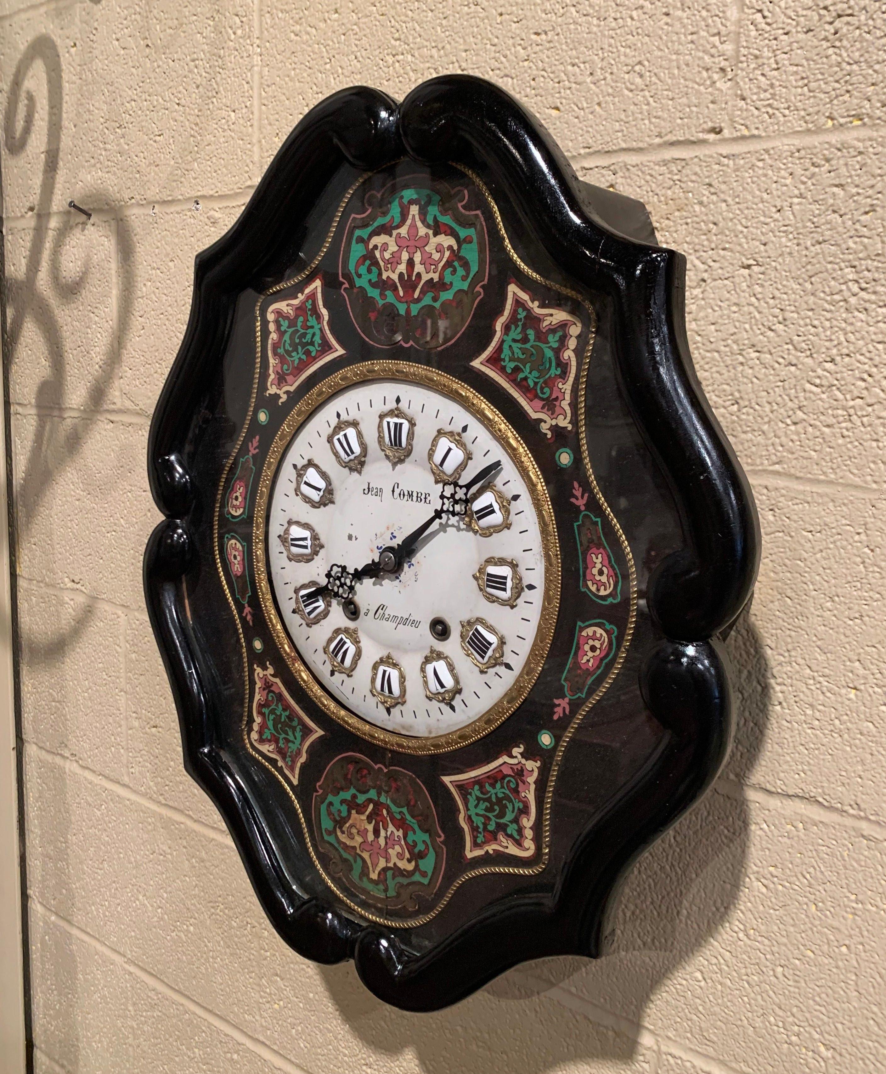 This elegant antique wall hanging clock was crafted in France circa 1870, oval in shape, the clock is ebony hand painted around the perimeter, the time keeper features colorful hand painted floral motifs on the facade under the glass top and around