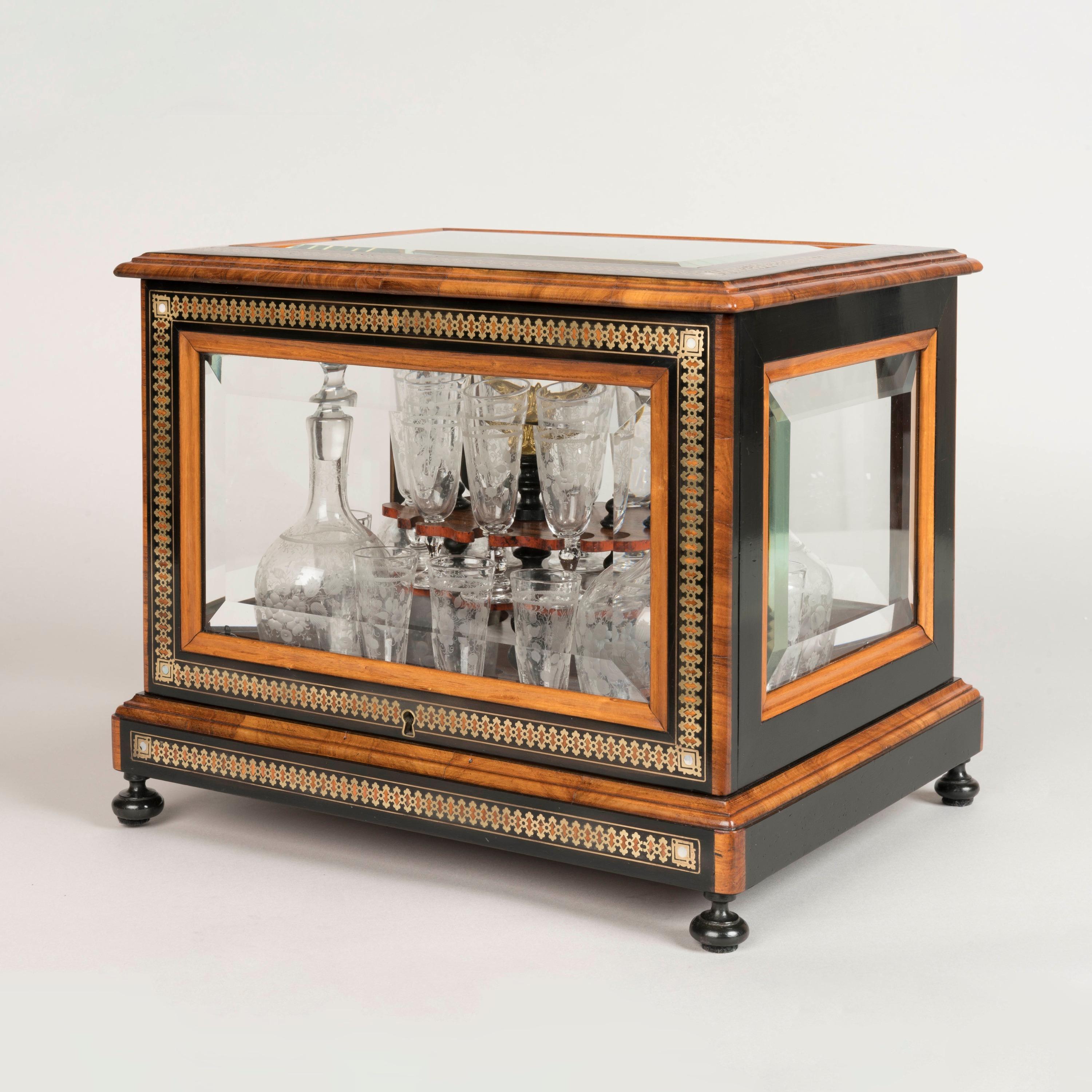 Cave à Liqueur en marqueterie Napoléon III

Objet décoratif et convivial du XIXe siècle, le coffret finement plaqué de noyer, de bois noirci, les côtés et le dessus en verre biseauté dans des cadres en marqueterie de laiton et de nacre, la boîte à