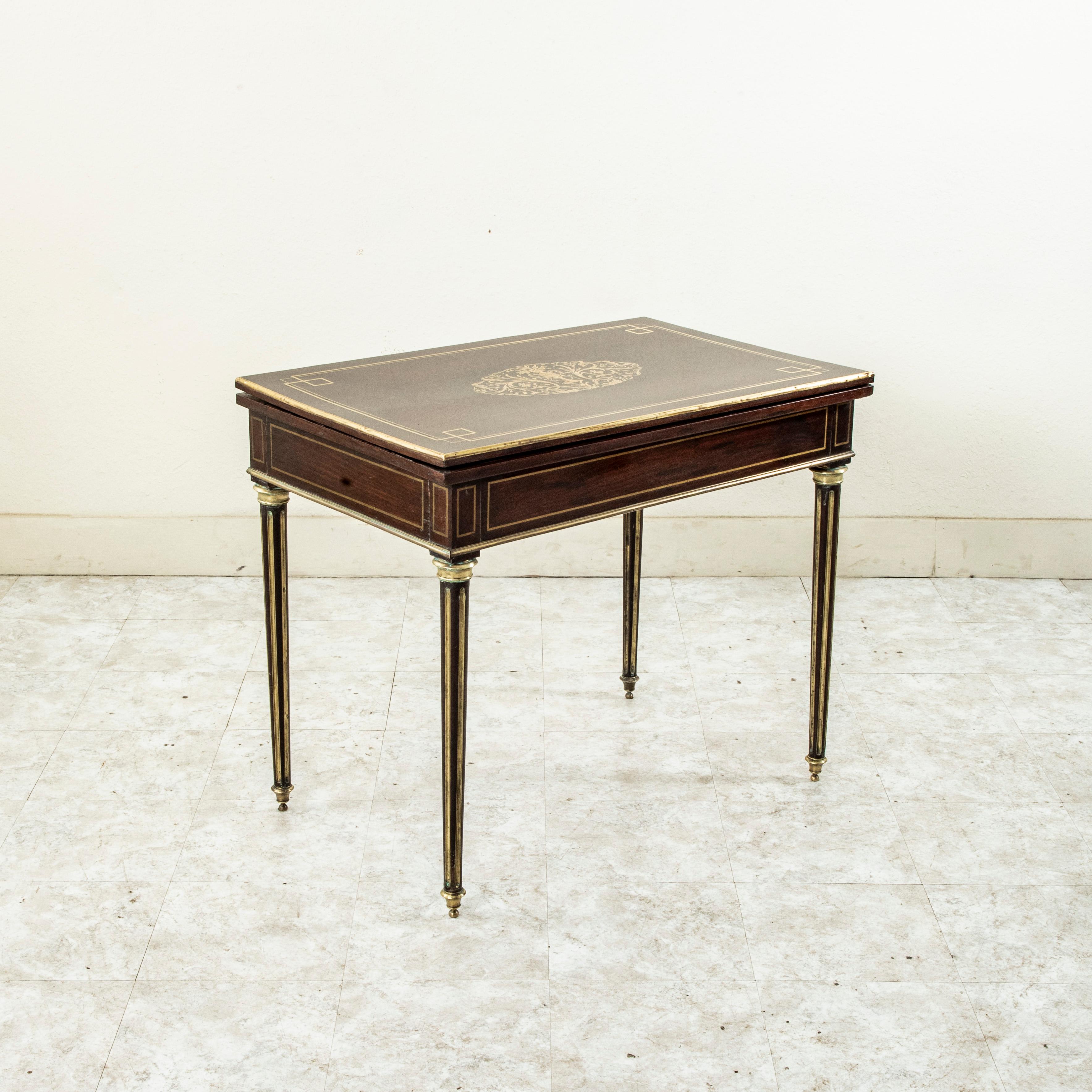 This mid nineteenth century French Napoleon III period mahogany game table features bronze inlaid trim inset on all sides and on the top. A central bronze inlaid urn with intricately scrolling leaves and flowers details the tabletop. The table rests