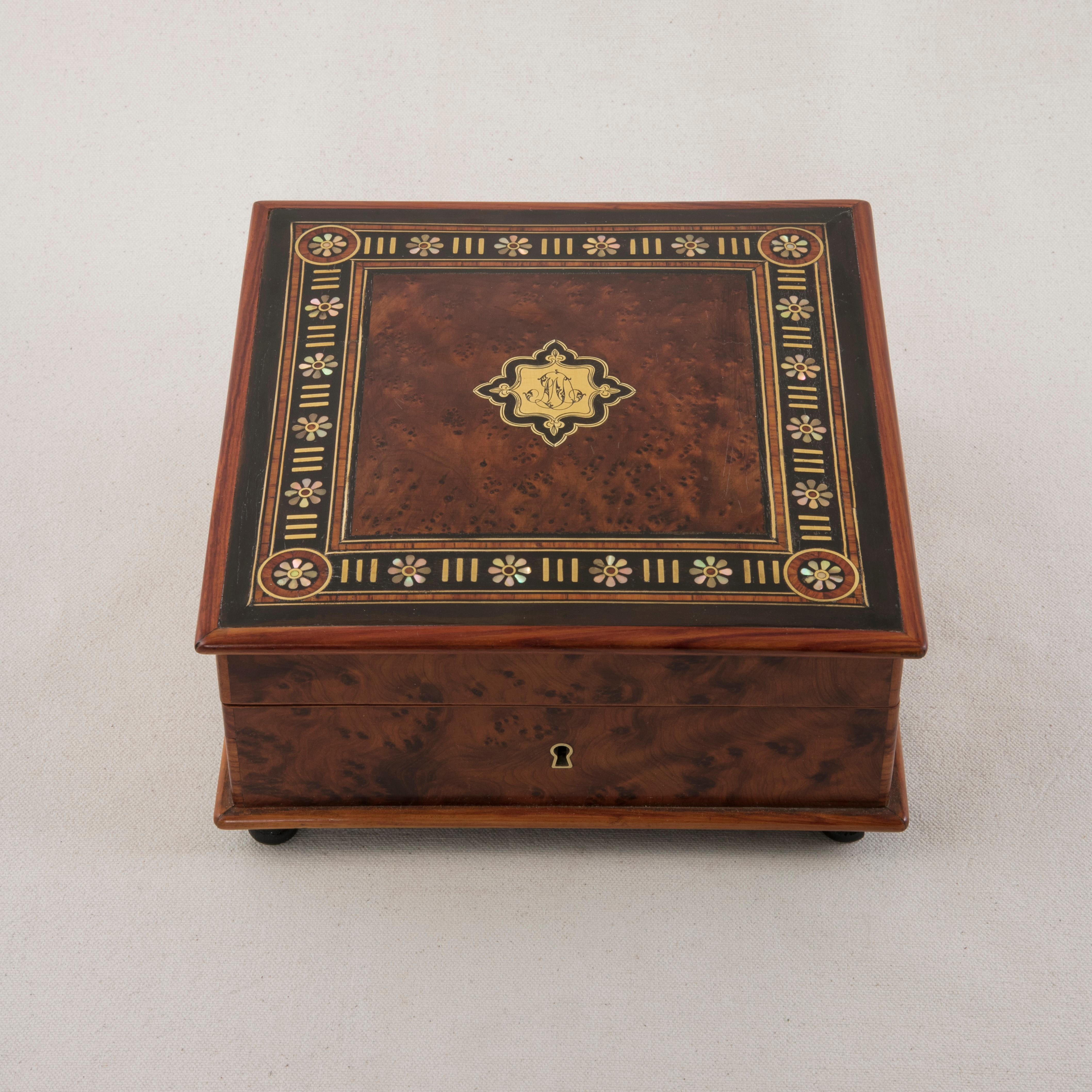 This mid-19th century French Napoleon III period box features an intricately inlaid marquetry top. The main form is constructed of thuya wood framed by rosewood. The lid displays a central bronze cartouche monogrammed MD and surrounded by ebonized