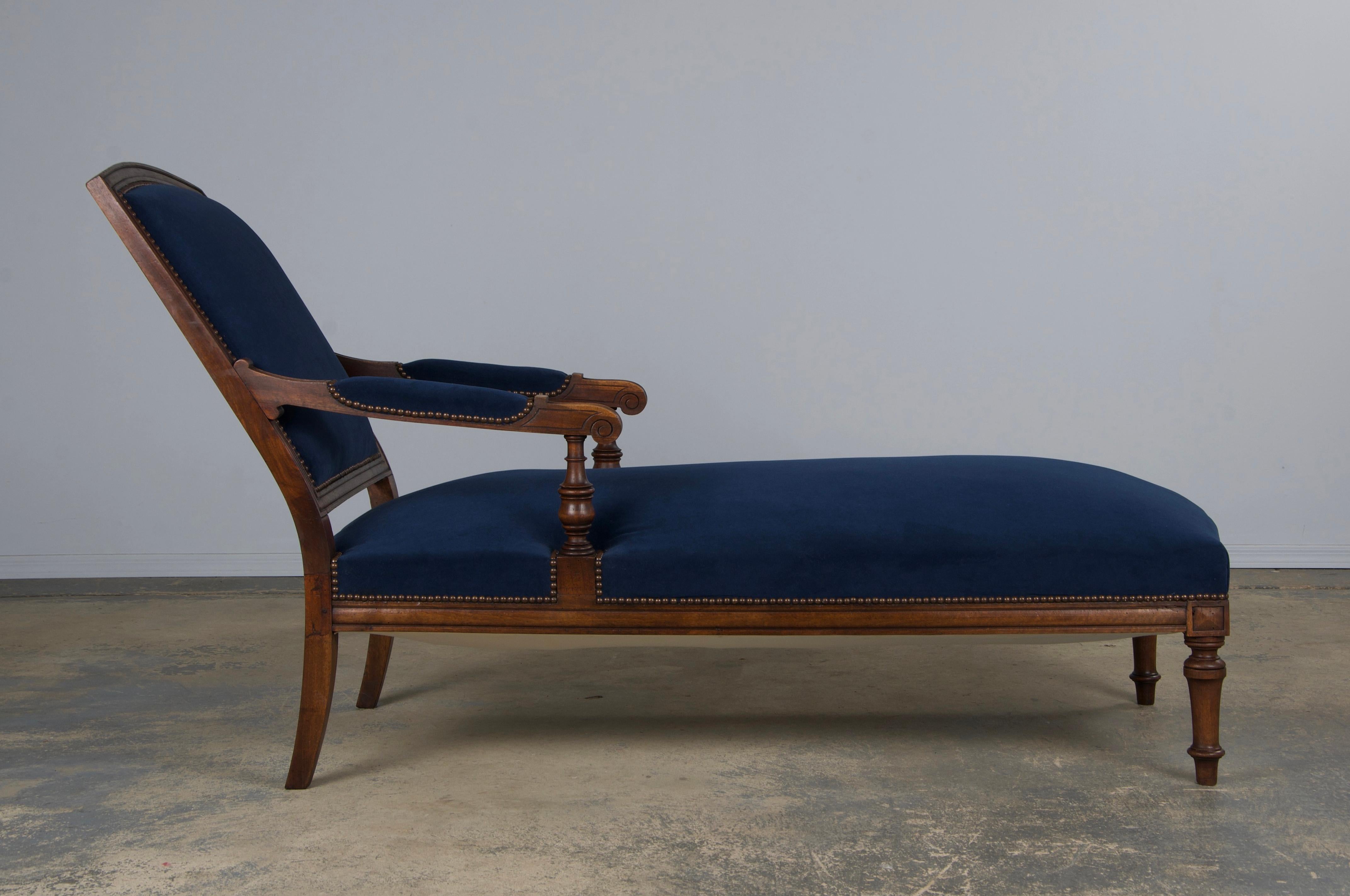 A fully restored mid-19th-century Napoleon III chaise lounge, sourced from Paris, France. Expertly handcrafted from solid walnut, it features a refined square back and gracefully hand-carved arms. The chaise has undergone a complete structural