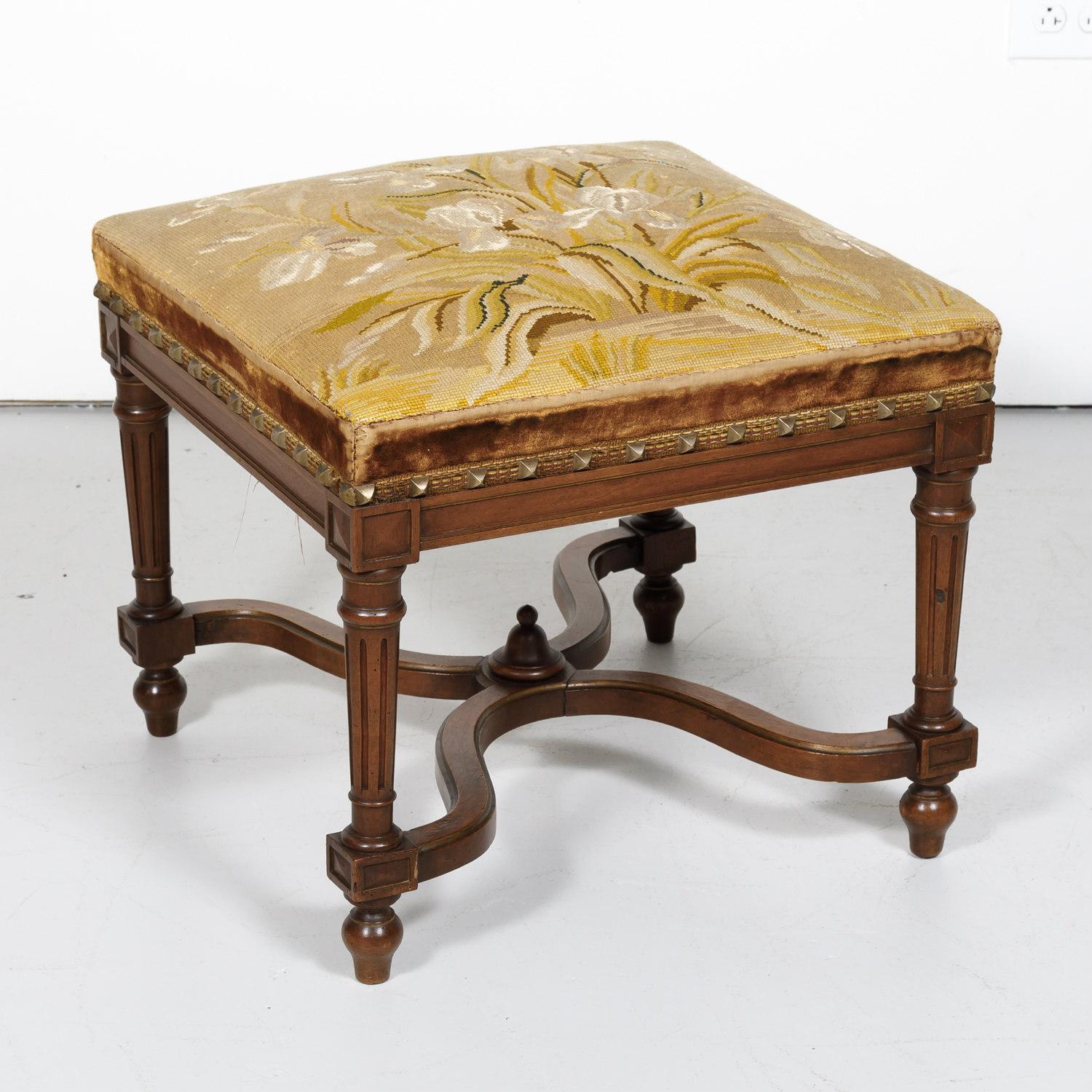 A lovely French Napoleon III period footstool handcrafted of walnut in Normandy having a beautiful floral needlework seat embellished with a velvet trim and brass nailheads, circa 1880s. Raised on fluted, tapering legs joined by a curved, carved 