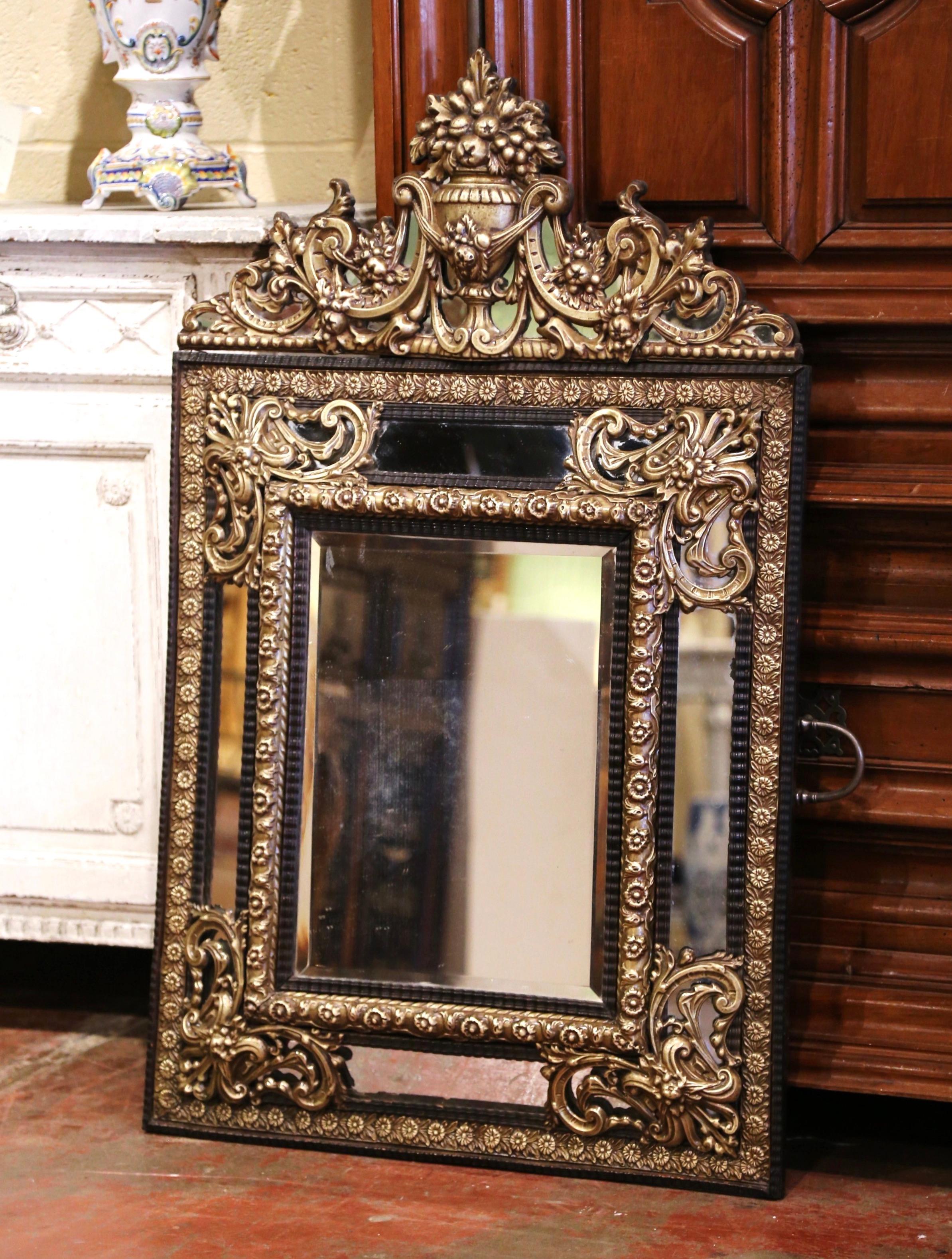 Created in France, circa 1870, the elegant antique wall mirror is decorated with intricate repousse decor including a cartouche at the pediment featuring a floral vase with foliage and scrolled motifs in high relief on the sides. The center mirror