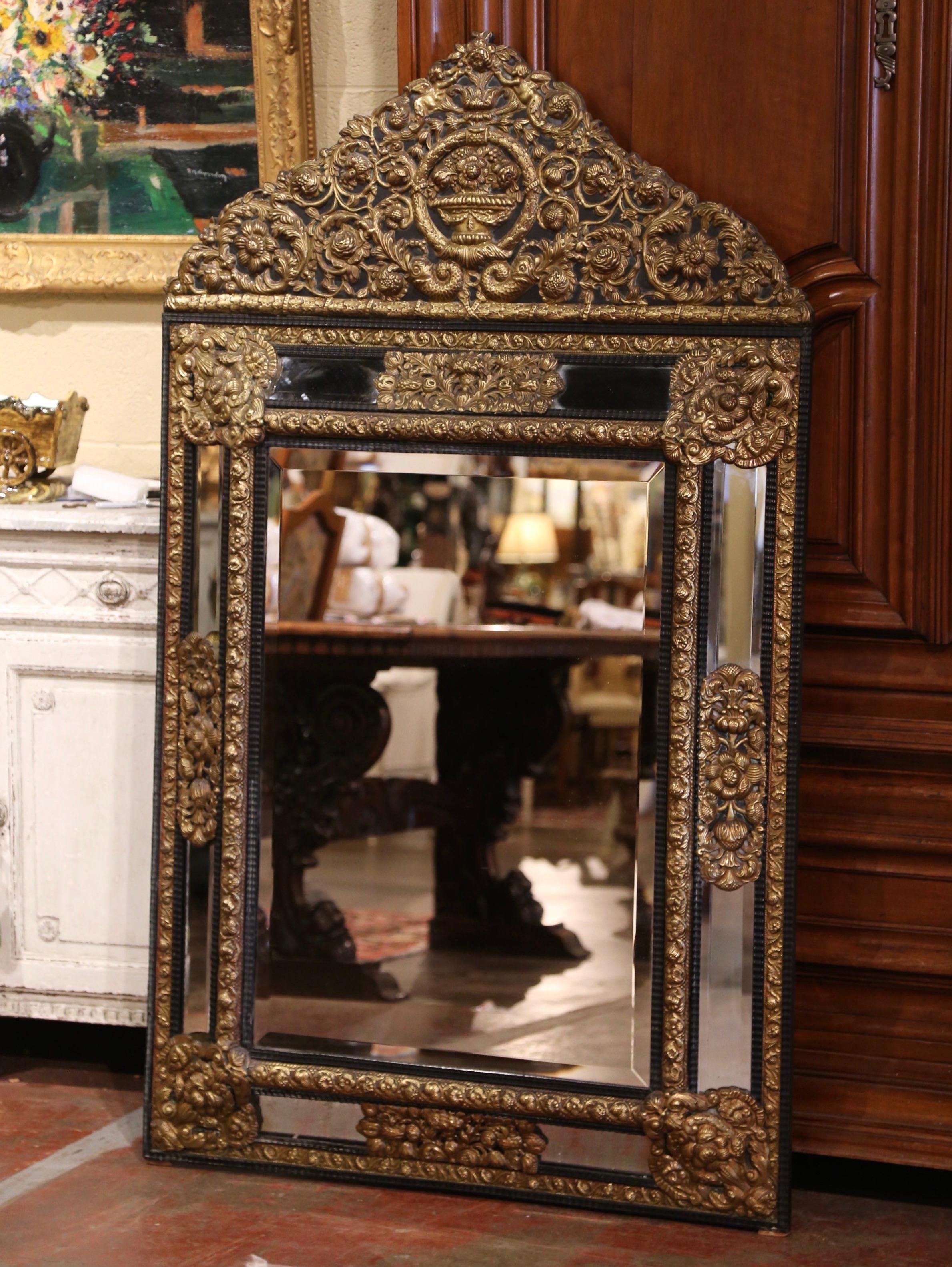 Created in France, circa 1870, the elegant antique wall mirror is decorated with intricate repousse decor including a very large cartouche at the pediment featuring a center floral vase with floral and fruit throughout, and flanked with cherub and