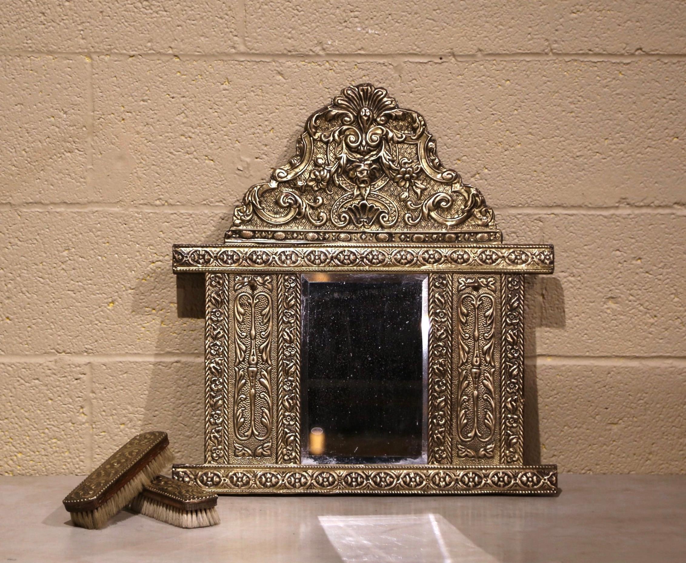 Created in France, circa 1870, the petite antique wall mirror is decorated with intricate repousse motifs including a cartouche with shell decor at the pediment. The mirror features the original beveled mercury glass with brushes on each side. Both
