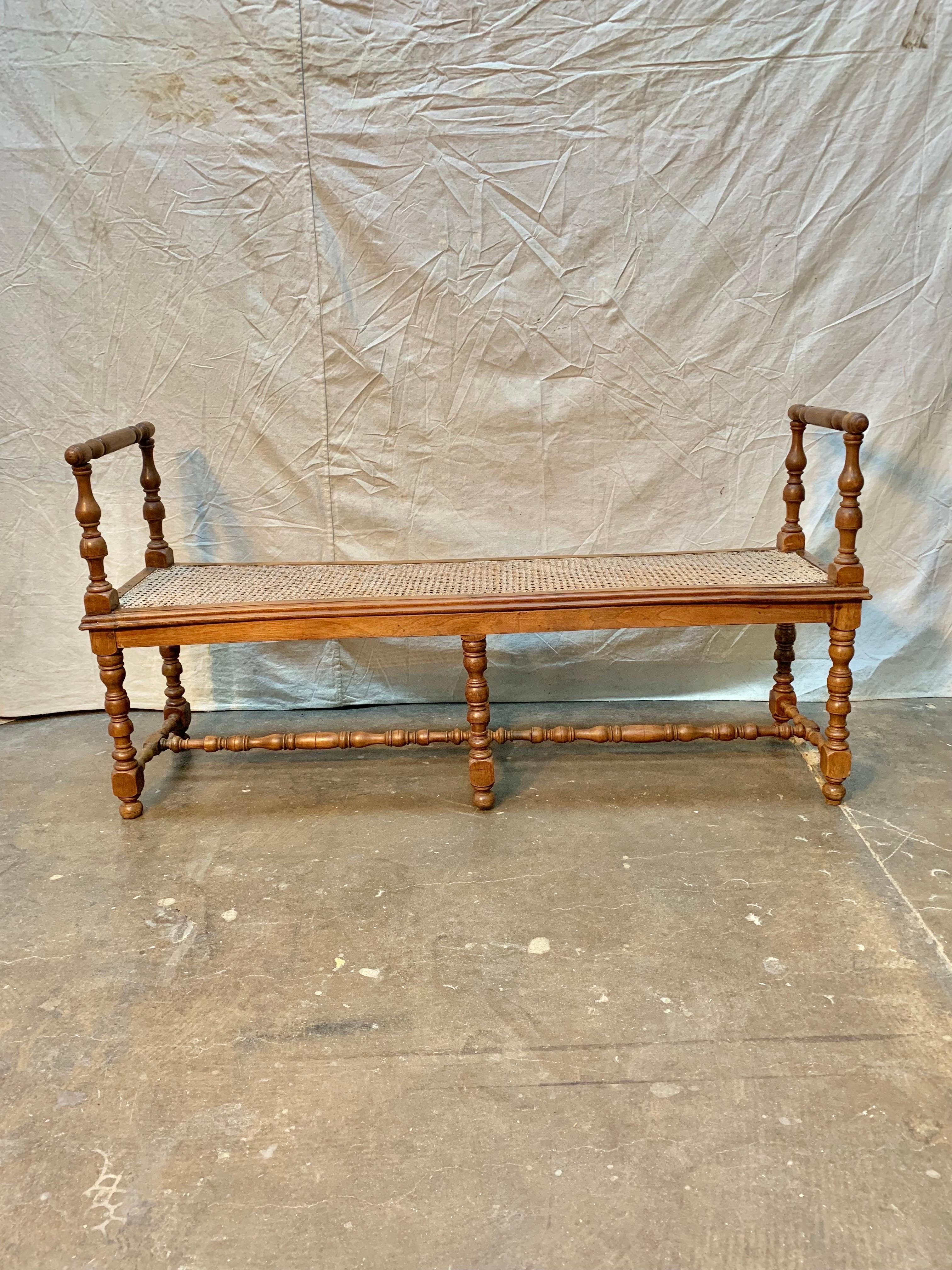 Found in the Burgundy region of France, this Napoleon III bench was crafted in the 19th century from old growth walnut and finished with a cane seat.  The piece features two open air turned armrests on each end that are attached to the wood framed