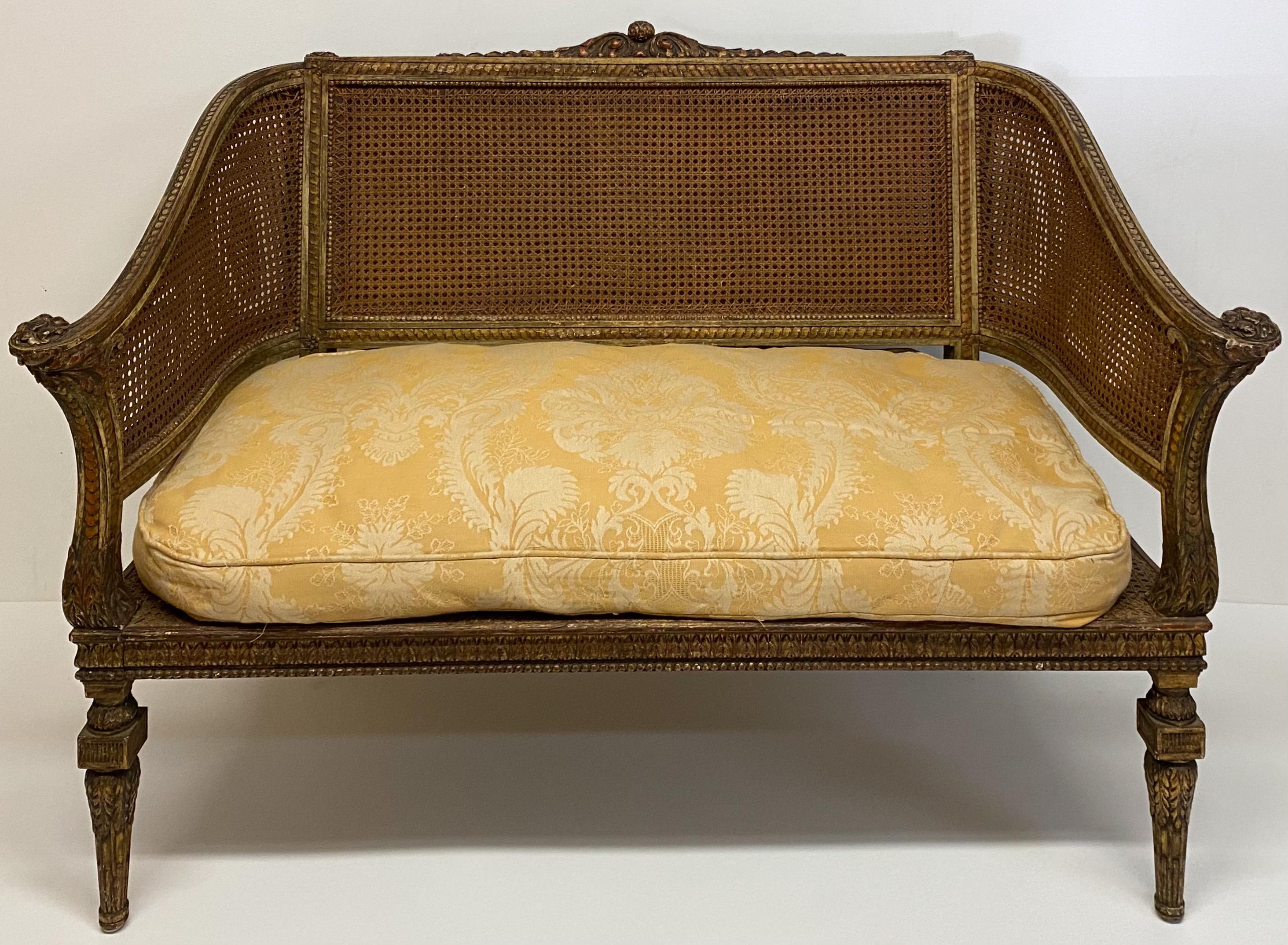 This is a wonderful piece! It is a French Napoleonic double caned and giltwood settee. The cane condition is marvelous with no pokes or tears. The down cushion is vintage and a damask raw silk. The patina is enhanced with the sloping carved giltwood
