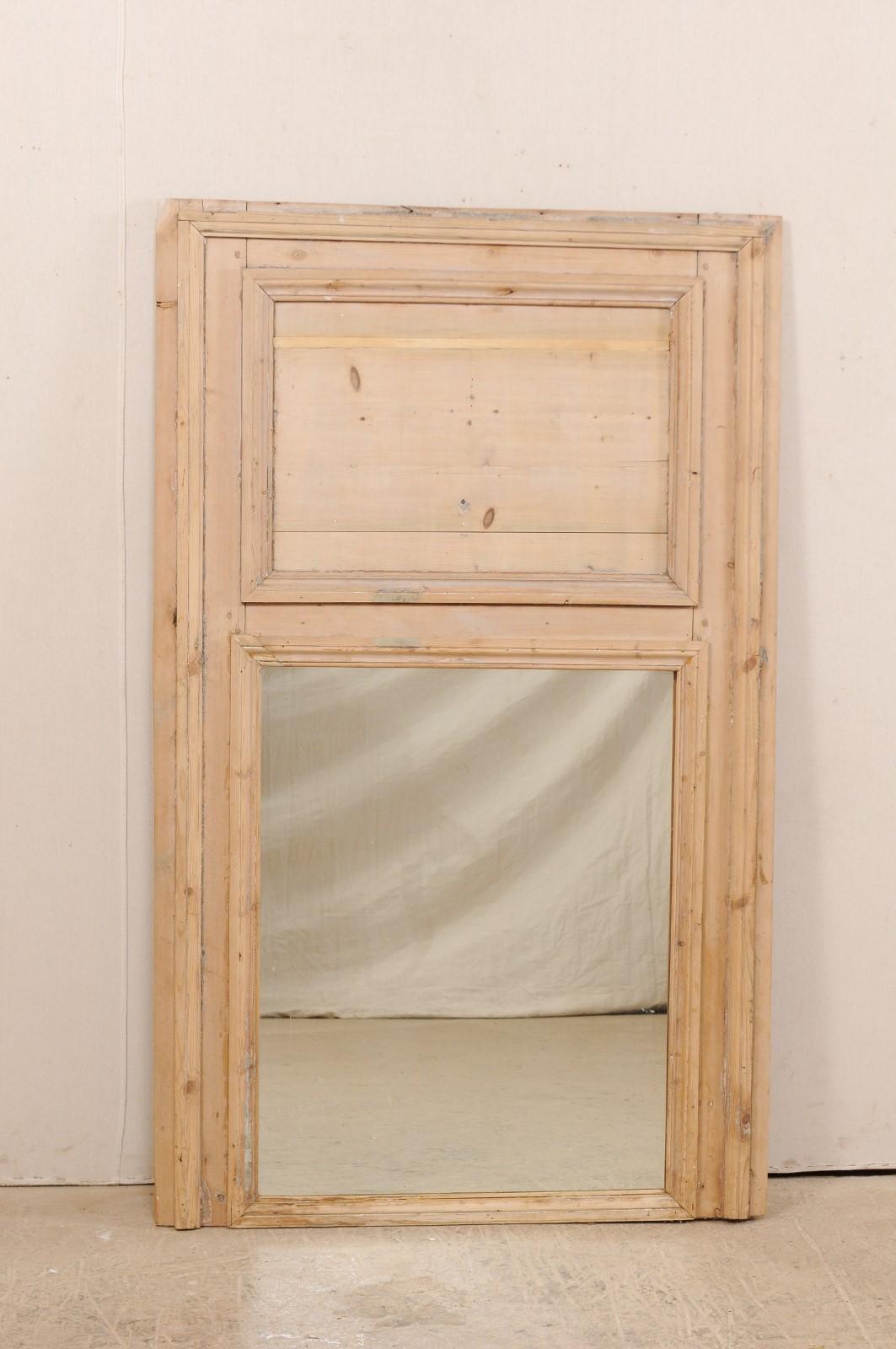 A French wooden trumeau mirror from the 19th century. This antique mirror from France features a vertical rectangular-shape with straight-line trim molding, with typical trumeau design of wooden plaque-style top over mirror below. It stands just