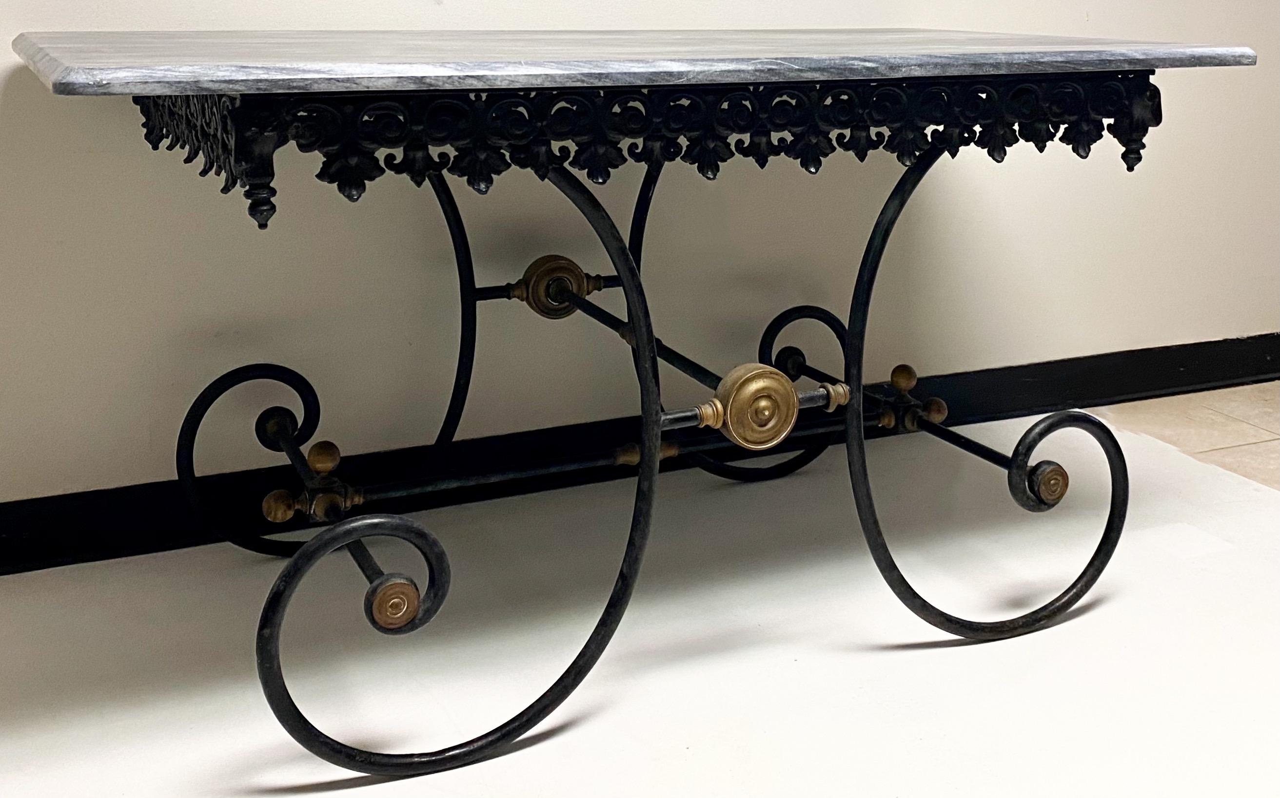 This is a 19th century French neoclassical cast iron and marble top baker’s table. The frame’s construction is a heavy cast iron and solid brass with ram’s heads on all four corners. The marble is most likely not original but is gray with white
