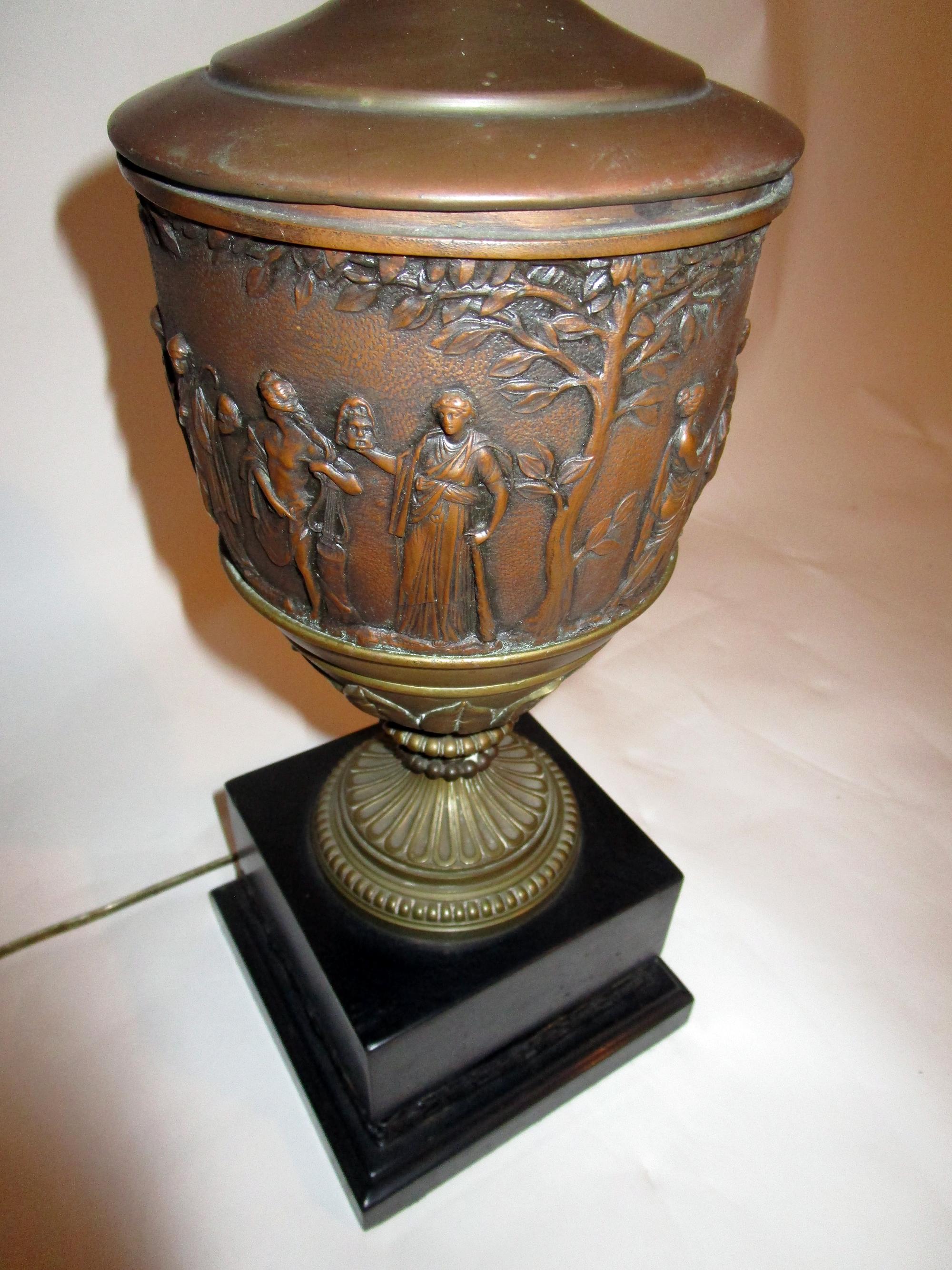 Handsome patinated brass urn converted into a lamp. Four laurel trees and ten different male and female figures, all in classical dress, in circle the urn which includes a pedestal of laurel leaves. The urn in mounted on an onyx square plinth with a