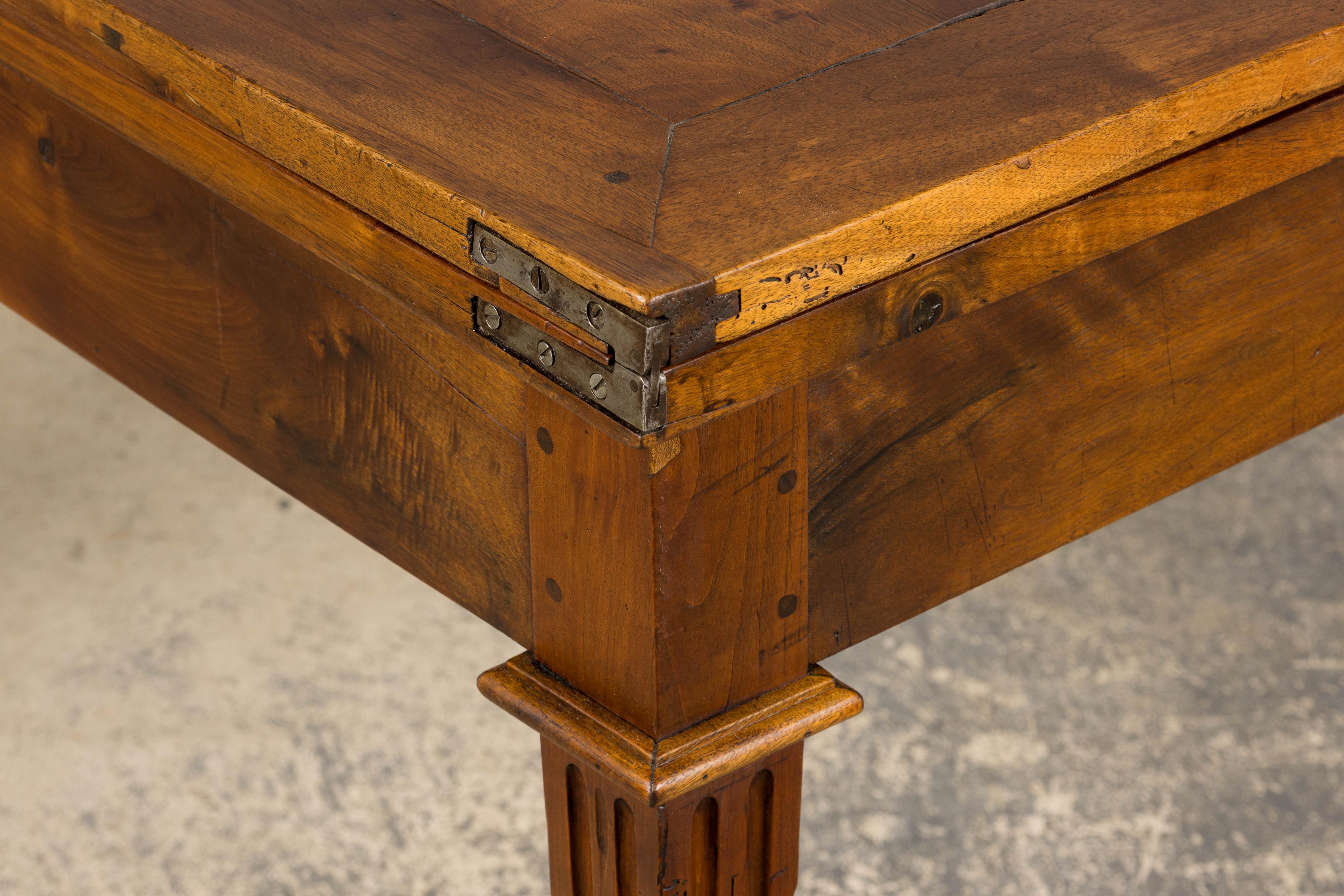 Mid-19th century French extendable dining table in the Neoclassical Louis XVI style, sourced from Provence, France. Hand-crafted from solid walnut, the table presents a rectangular folding top with original metal hinges that pivots smoothly around a