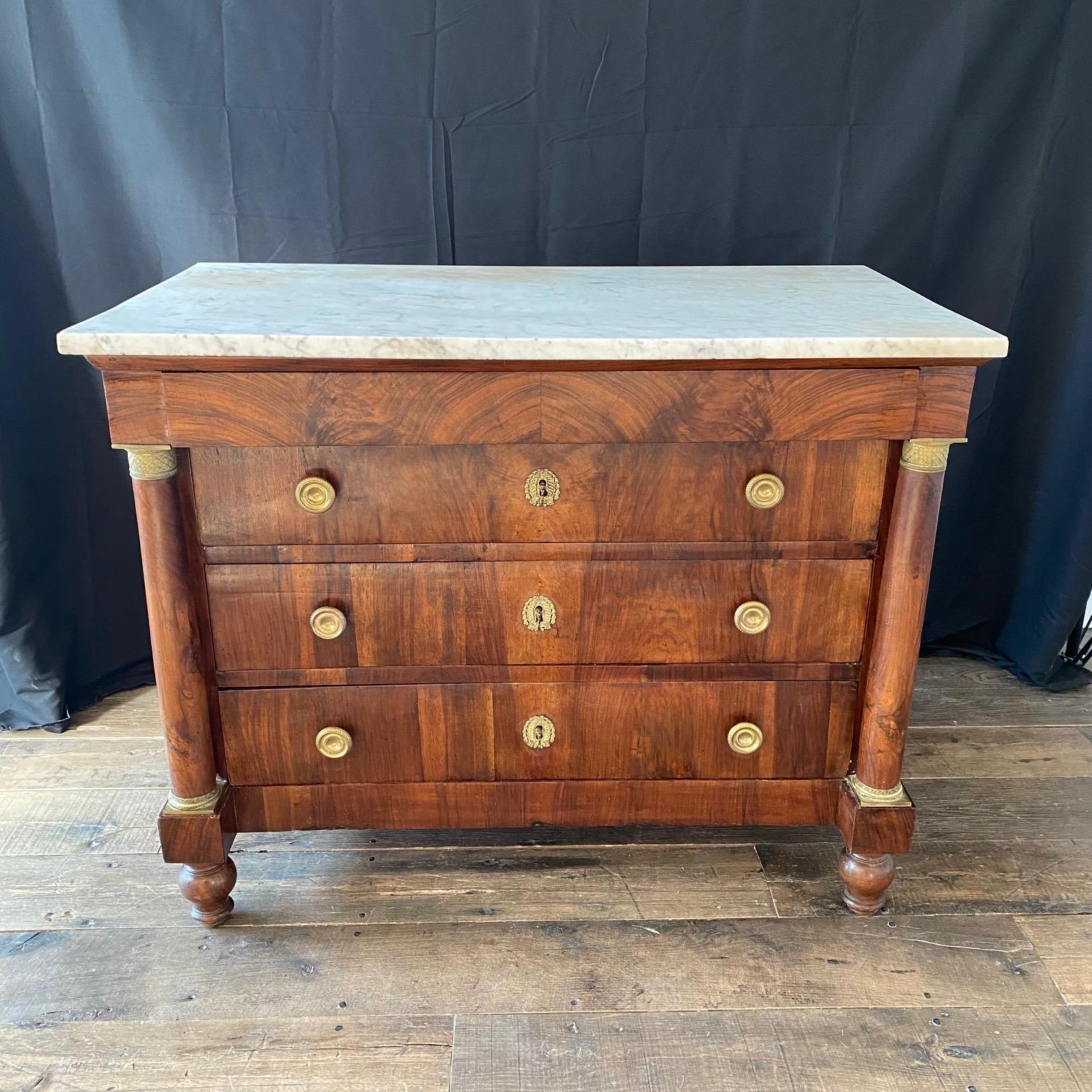 A French Neoclassical commode with marble top and exquisite brass accents.  This antique chest  features a rectangular-shaped Carrara marble top, over case which houses four drawers (upper drawer is disguised within the top frieze), flanked within a
