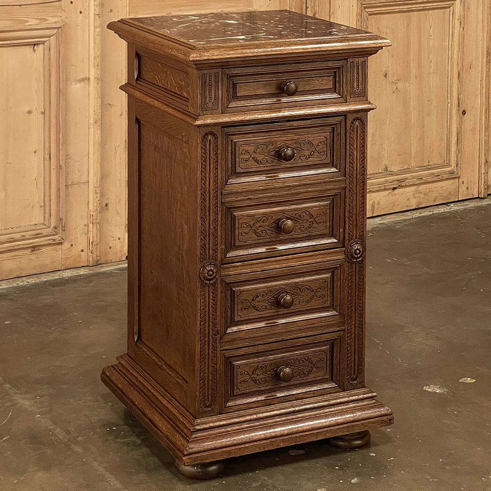 19th Century French Neoclassical marble top nightstand was fashioned from solid oak, and features tailored architecture embellished with fletching and rosettes on the cornerposts, and intaglio scrollwork on all the front facade panels. The top panel