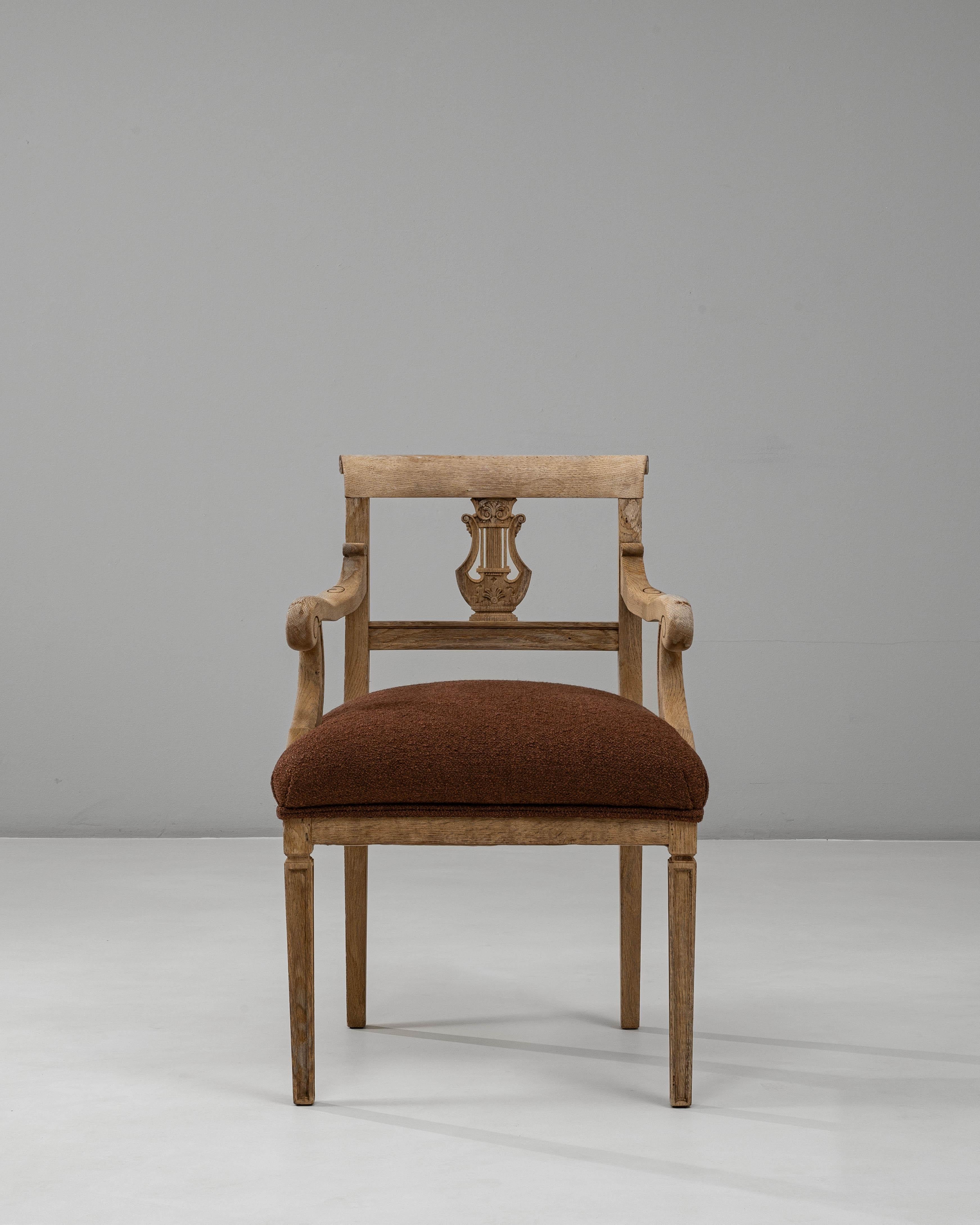 This 19th-century French Neoclassical oak armchair exemplifies refined craftsmanship and timeless elegance. The carved lyre motif on the backrest highlights classical inspiration, while the gracefully scrolled arms and fluted legs add architectural