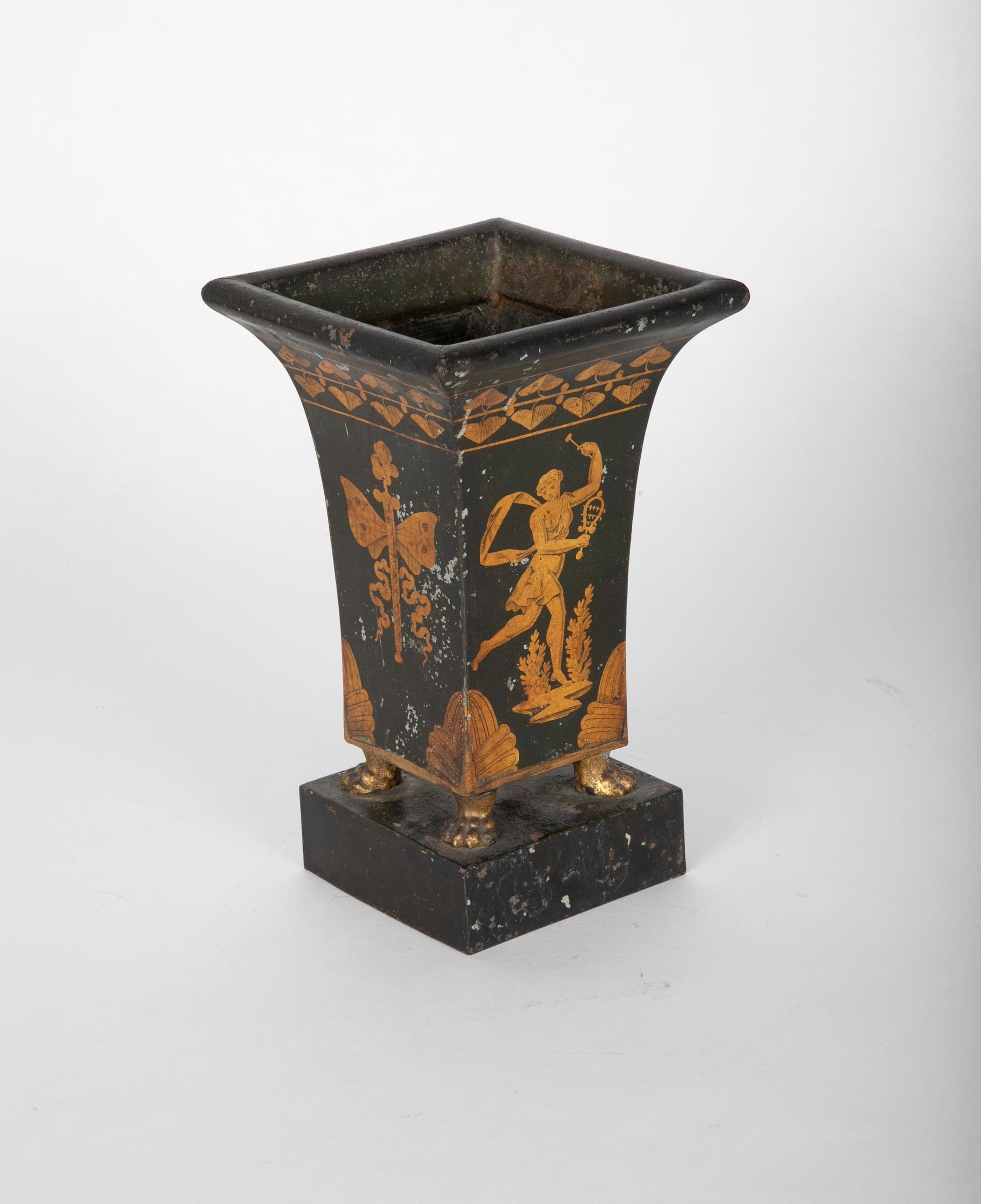 A very charming early 19th century French tole peinte vase or urn with a gilt figure of a dancing maiden with one breast exposed playing a sistrum, ancient musical instrument. The urn supported on a rectangular plinth by four gilt lion paw feet. The