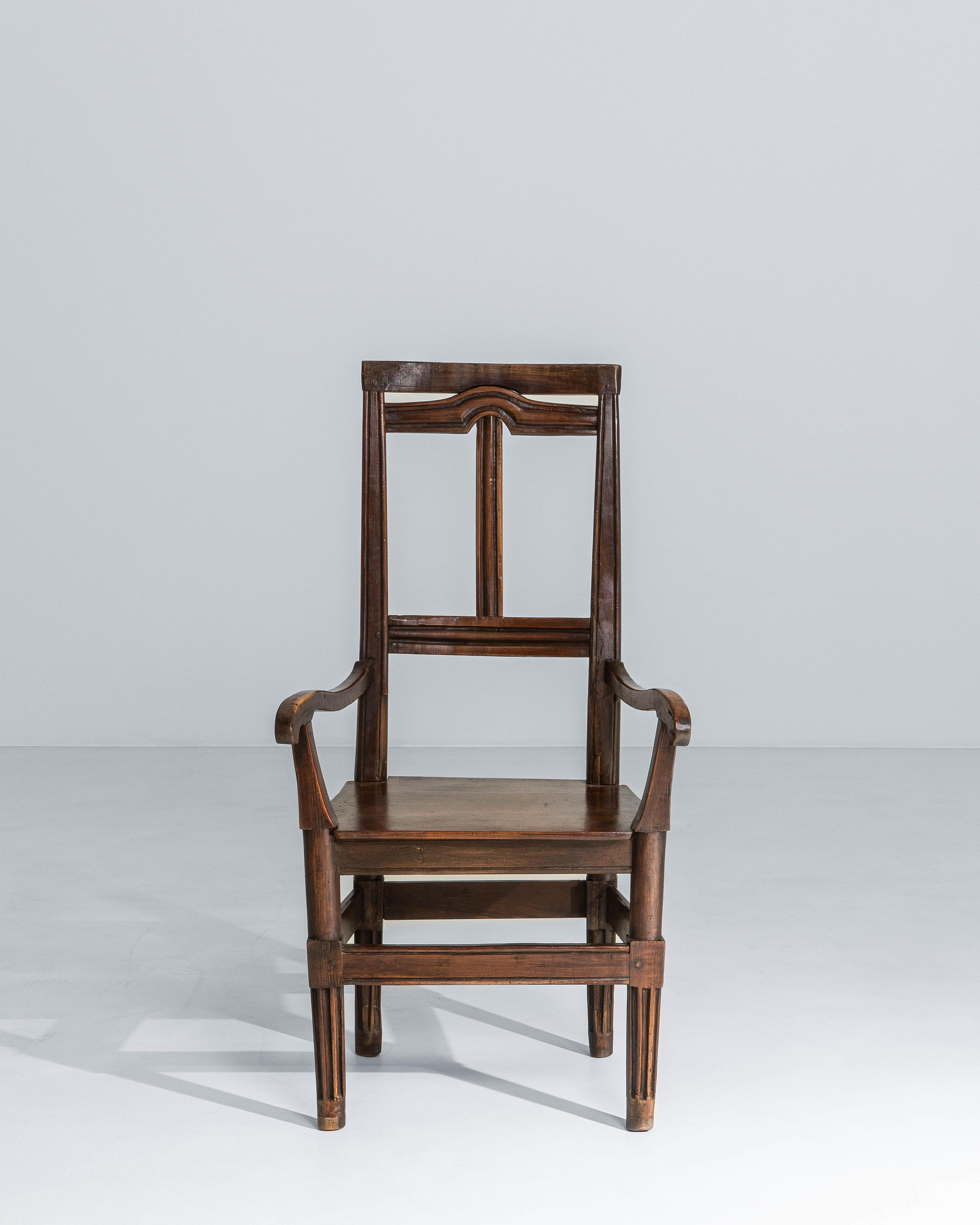 This 19th century French Neoclassical walnut armchair reflects the restrained elegance and architectural clarity of the period. Crafted from solid walnut, the chair features a tall, rectilinear back with subtle stepped moldings that echo classical