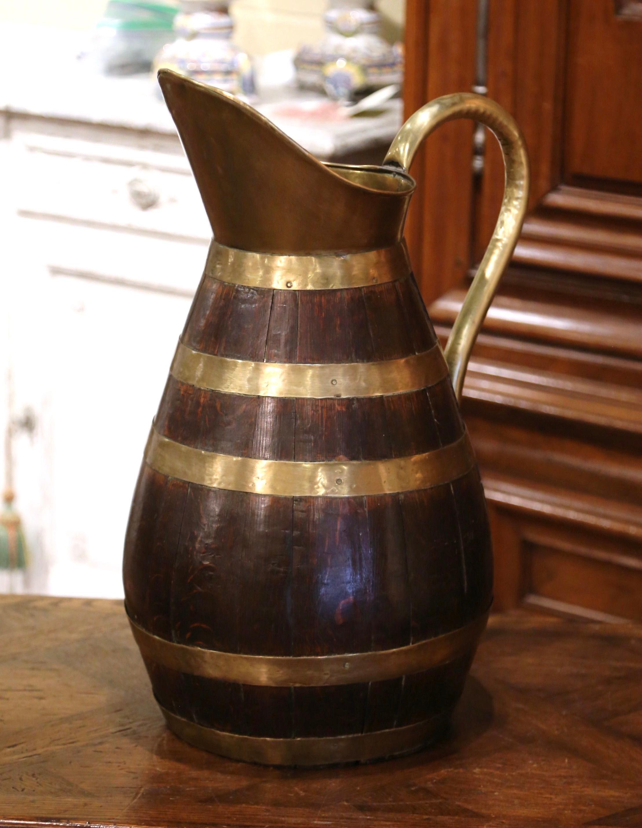 Accessorize your wine cellar or wet bar with this antique cider pitcher jug; crafted in Normandy France circa 1870, the pitcher is made of barrel oak decorated with polished brass rings. The cider pitcher, further embellished with a brass handle, is
