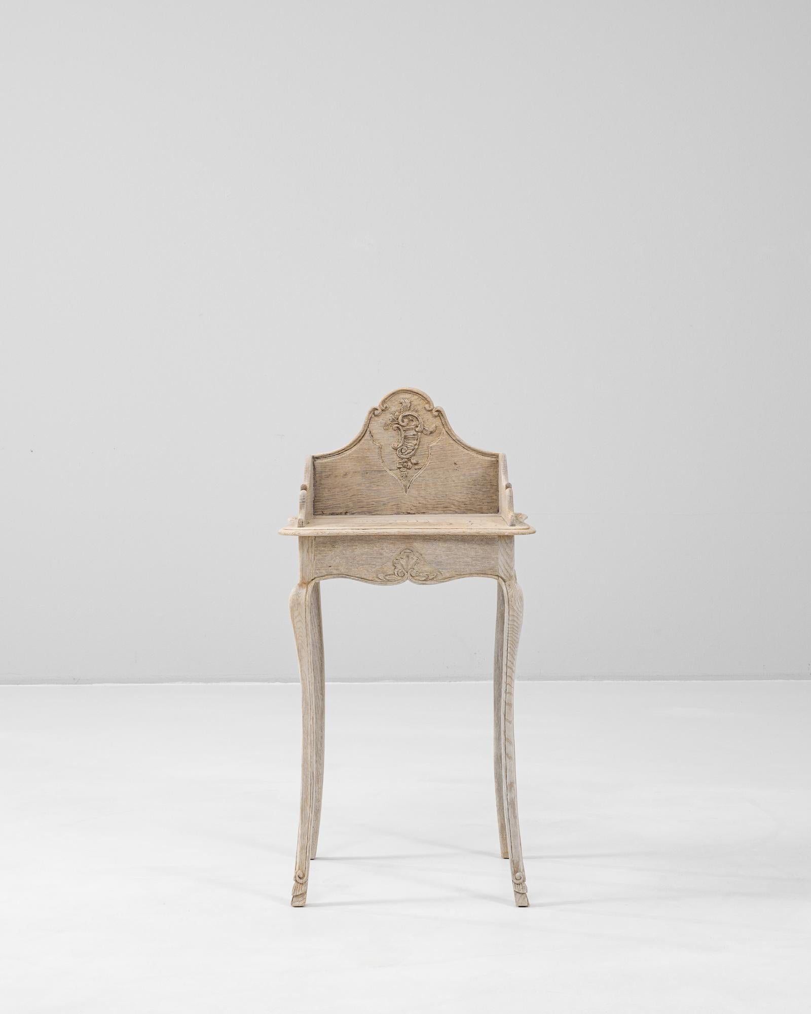 This 19th Century French Oak Bedside Table embodies the elegance of the Louis XV period with its graceful curves and detailed carvings. Crafted from solid oak with a pale, natural patina, the table features a scalloped apron, carved shell motif, and