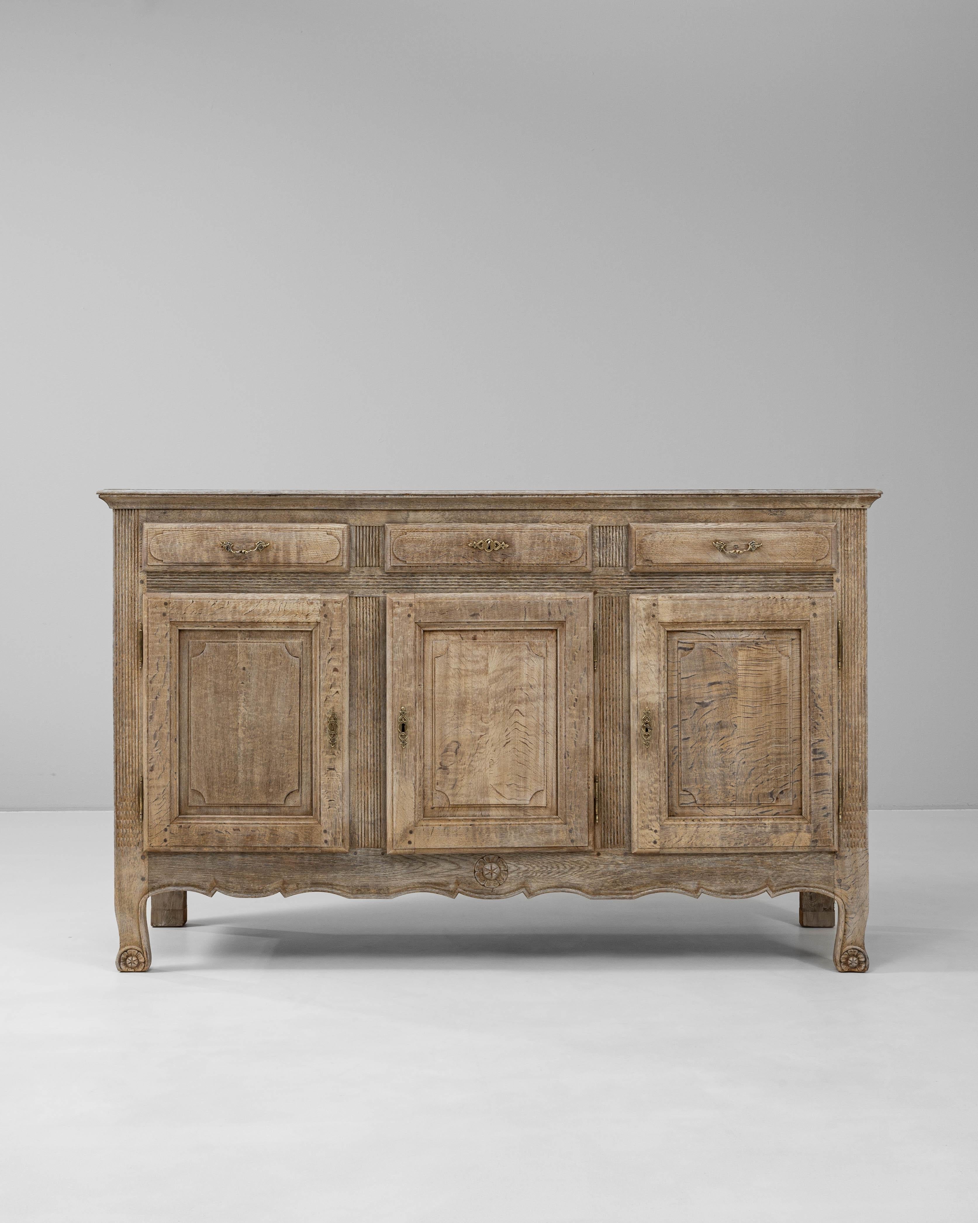 This 19th Century French oak buffet showcases the graceful balance of rustic charm and classical detail typical of the period. Crafted from solid oak, the piece features three paneled doors below a trio of drawers, offering generous storage for