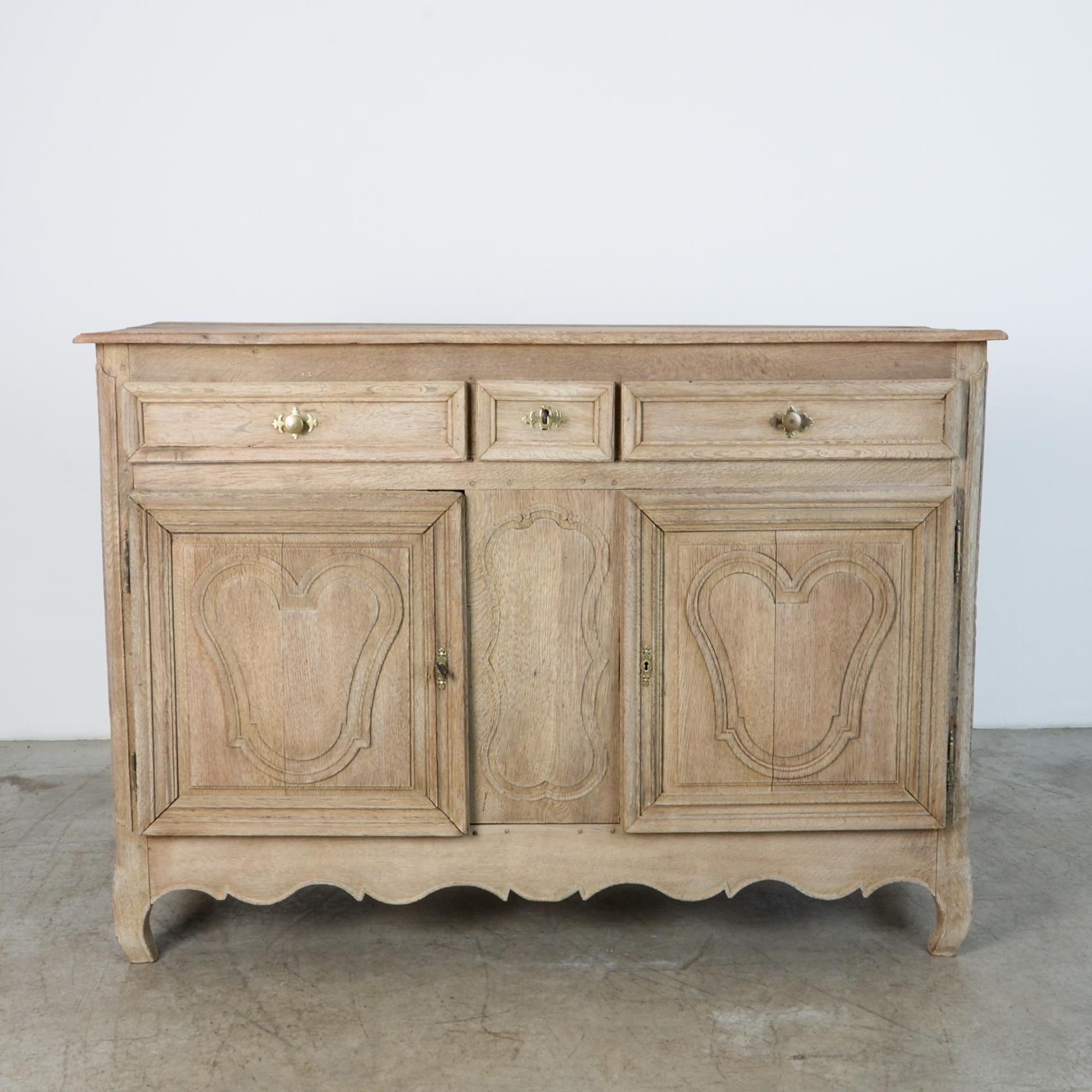 An oak buffet from France, circa 1860. Handles and locks are fully functional casted brass with beautiful worn patina. Carved drawer panels, underlined by an elegant carved apron.

The bleached oak finish is achieved through the application of