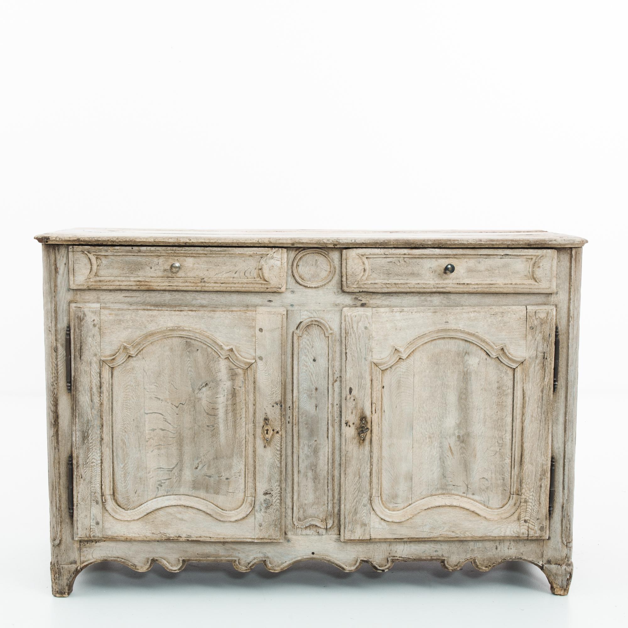 An oak buffet from France, circa 1820. The upright frame is enhanced with subtle rococo stylings: the embellished curve of the door panelling, the scalloped apron, the slight cabriole of the feet. The wood has been restored to a natural finish,