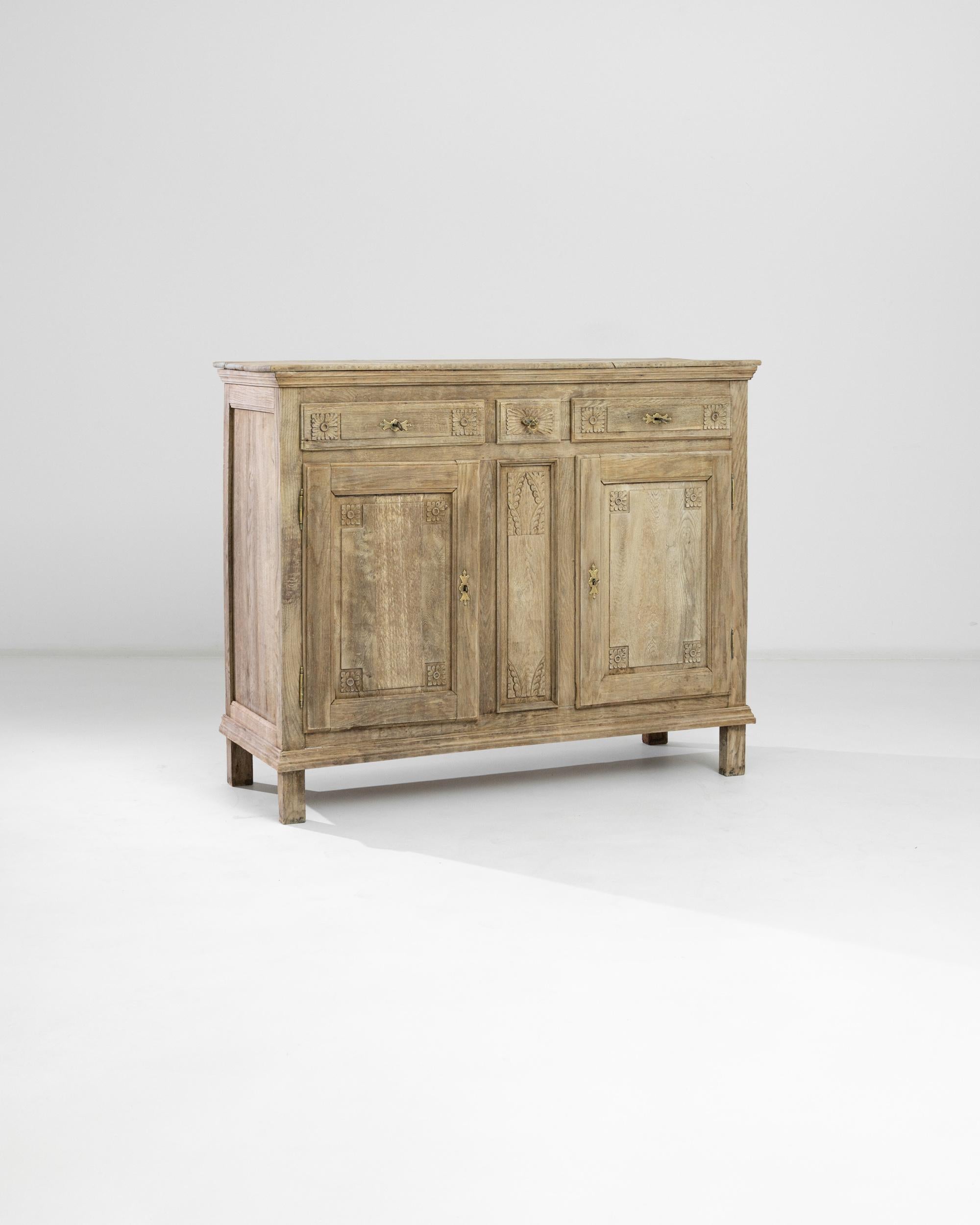 A bleached oak buffet handcrafted in France circa 1860. This vintage chest boasts delicately carved nature-inspired geometrical ornaments that adorn the corners of drawers and panels with exquisite flower and foliage accents. The neoclassical