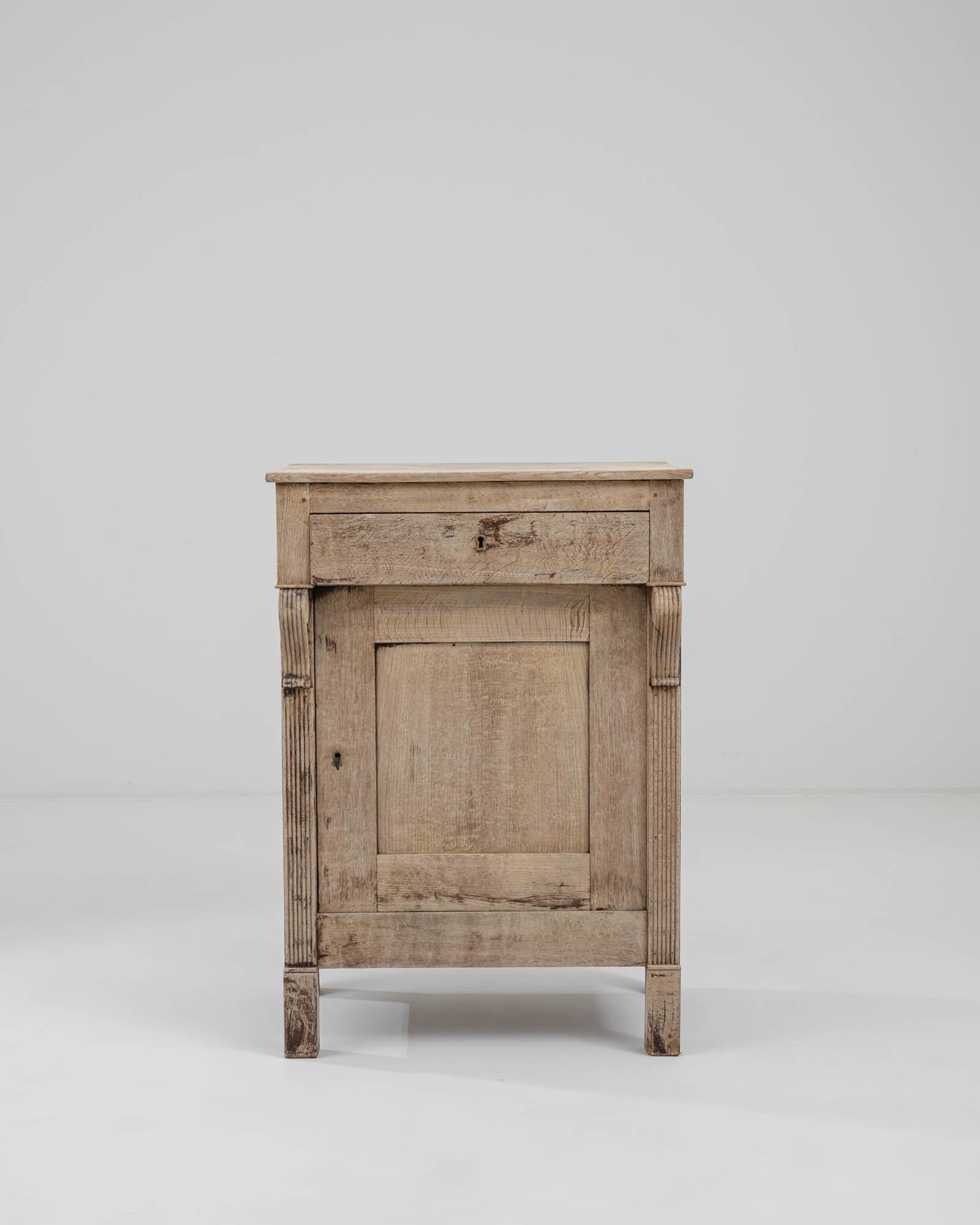 This delightful antique oak buffet combines a dignified Empire aesthetic with a bright natural finish. Made in France in the 1800s, fluted pilasters and an overhanging upper drawer lend an architectural majesty to the simple lower cupboard. Carved