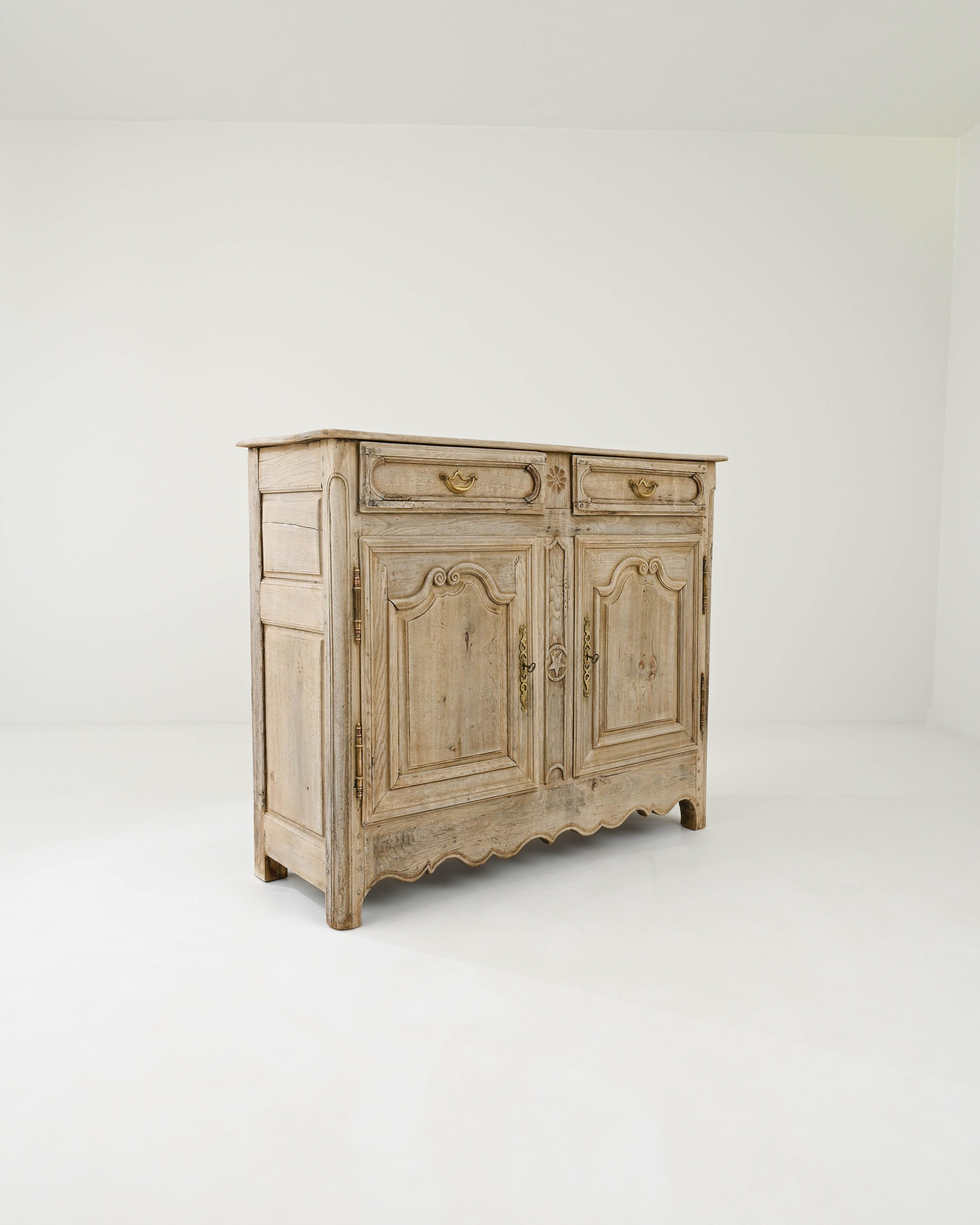 An oak buffet, hand-crafted in France during the 19th century. The blond tone of the bleached wood reveals a graceful rippling grain, highlighting masterfully carved details on the doors and a pair of drawers. The scalloped apron bestows the chest