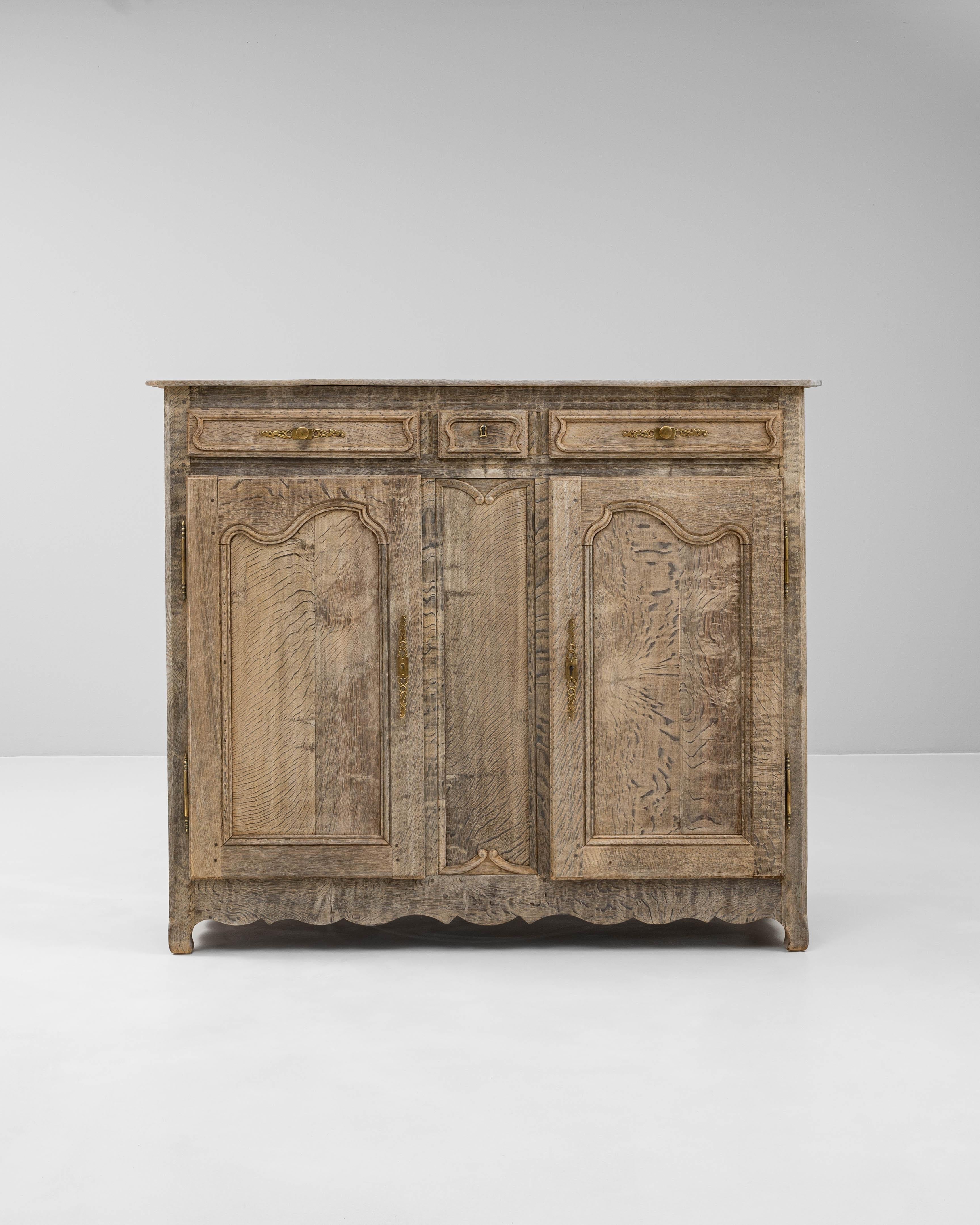This 19th Century French oak buffet is a refined example of provincial craftsmanship, featuring a beautifully bleached finish that enhances the natural movement of the grain. The piece offers a classic façade with three paneled doors below and three