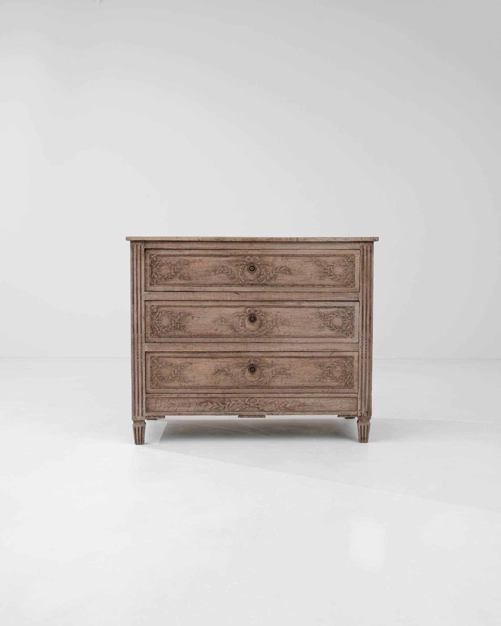 Artfully carved flower wreath carvings with ribbons, which adorn the front of this three-drawer chest crafted in 19th-century France, are exquisitely highlighted against the high-quality oak wood, flaunting a subtle warm hue. The central carvings