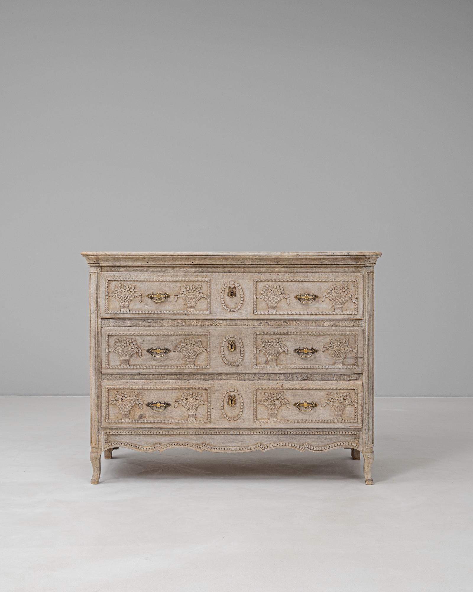 This 19th Century French oak chest of drawers is a beautifully carved example of Louis XVI style, featuring delicate neoclassical motifs and original gilt brass hardware. The front is richly adorned with symmetrical basket-of-flowers reliefs, framed