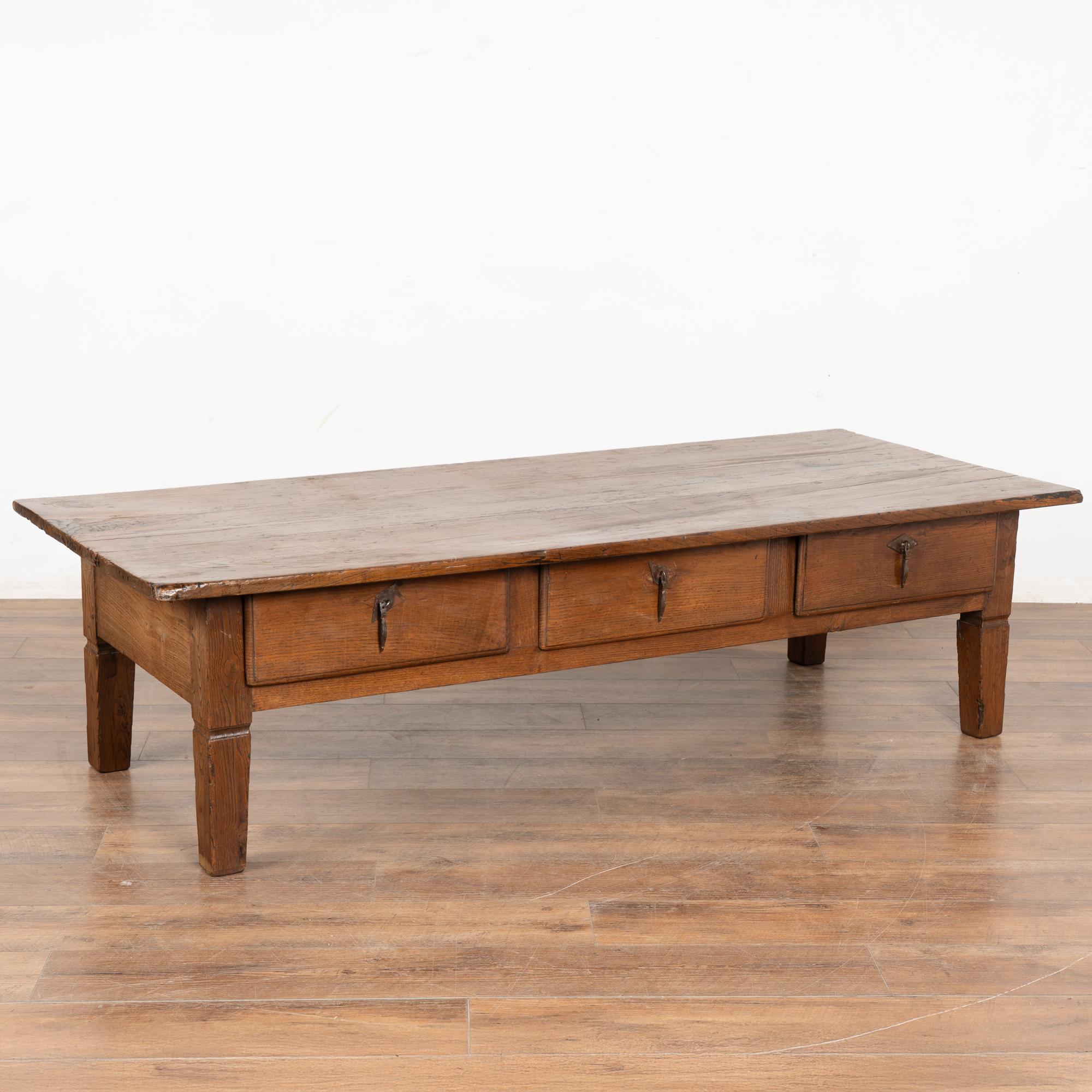 L'attrait de cette table basse provient de la riche patine du bois de chêne français usé. Chaque éraflure, entaille, fissure, tache et vieux trous de vers séchés ajoutent au caractère de cette table basse.
Trois tiroirs fonctionnels avec poignées en