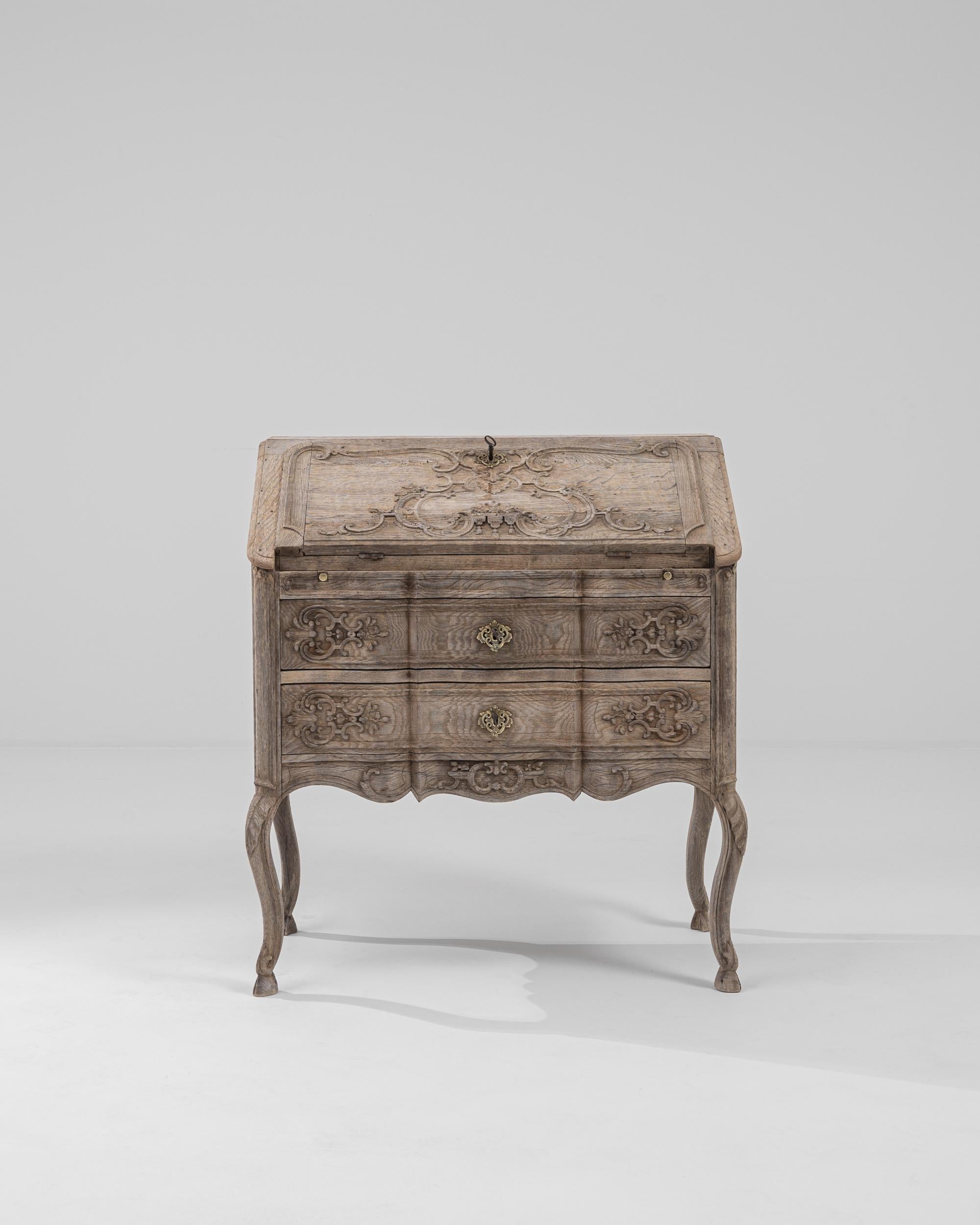 Made in France at the turn of the century, this beautiful writing desk in natural oak takes inspiration from the ornate escritoires of previous centuries—from the serpentine shape of the cabinet to the elaborate carved relief of the paneling. Regal