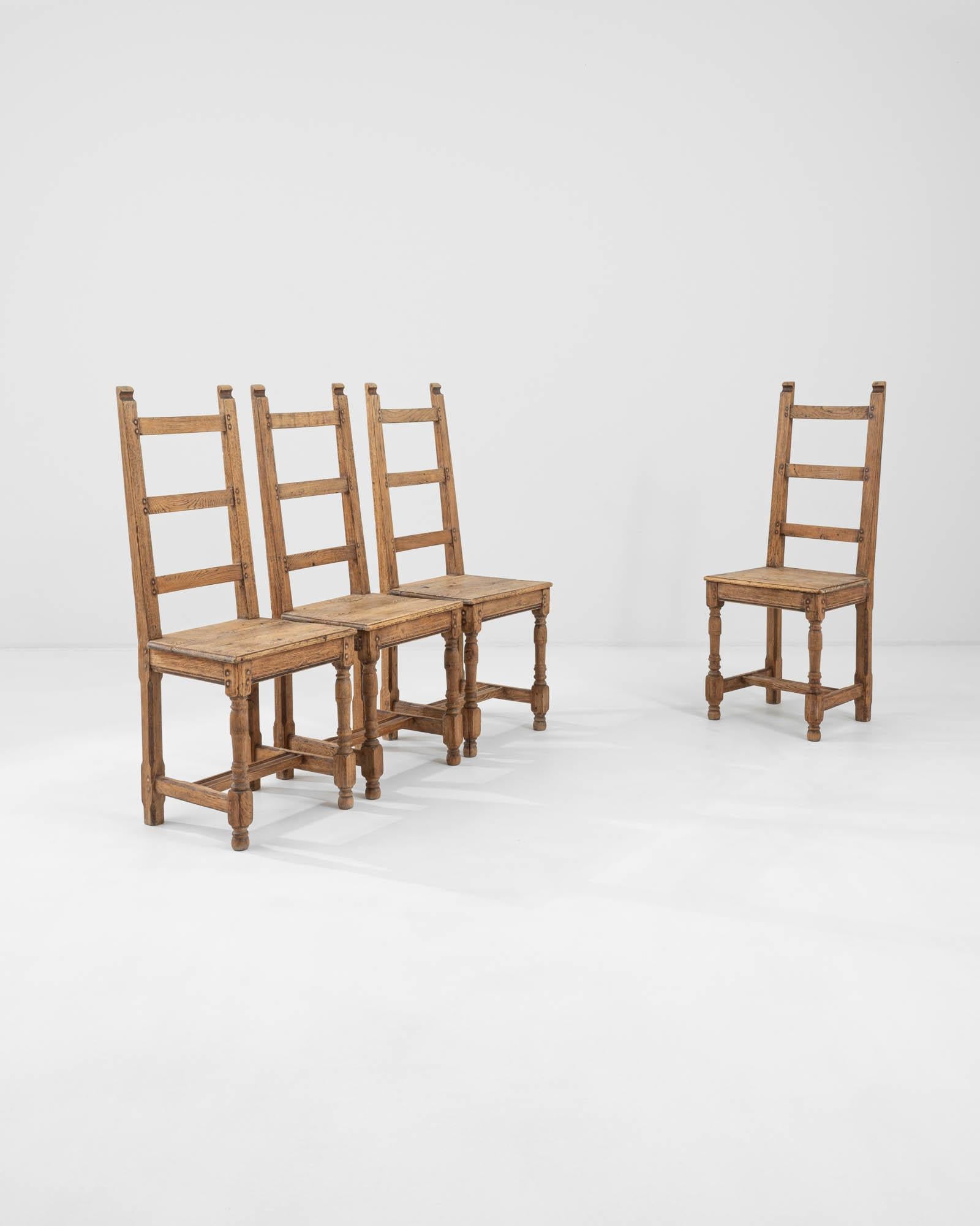 A set of wooden dining chairs created in 19th century France. Gleaming, rich brown hardwood composed into a thoughtful and utilitarian construction characterizes these chairs as a farmhouse style staple. Charming dowel rod pegs, notched seat backs,