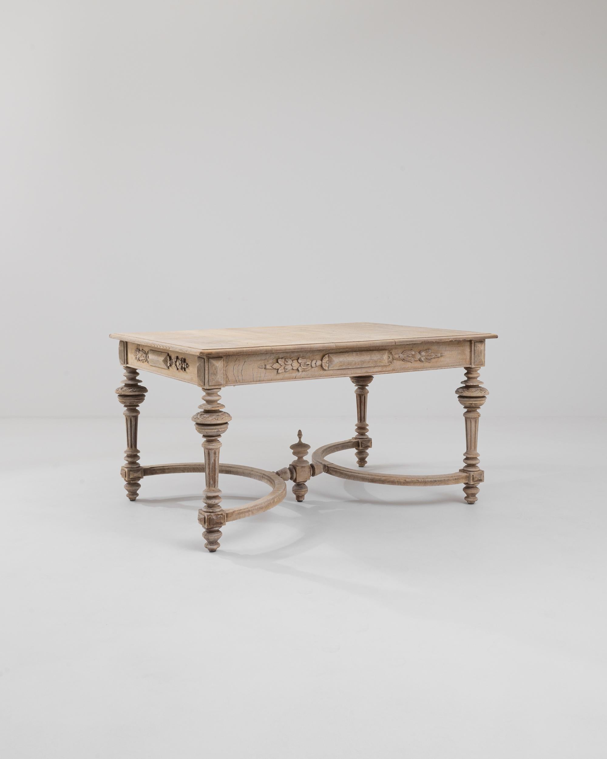 An oak dining table made in 19th century France. The swooping stretchers and beautifully lathed legs support a clean and unadorned oak top. Ornate floral motifs have been lovingly hand-carved into the aprons of the table, brought to new life by