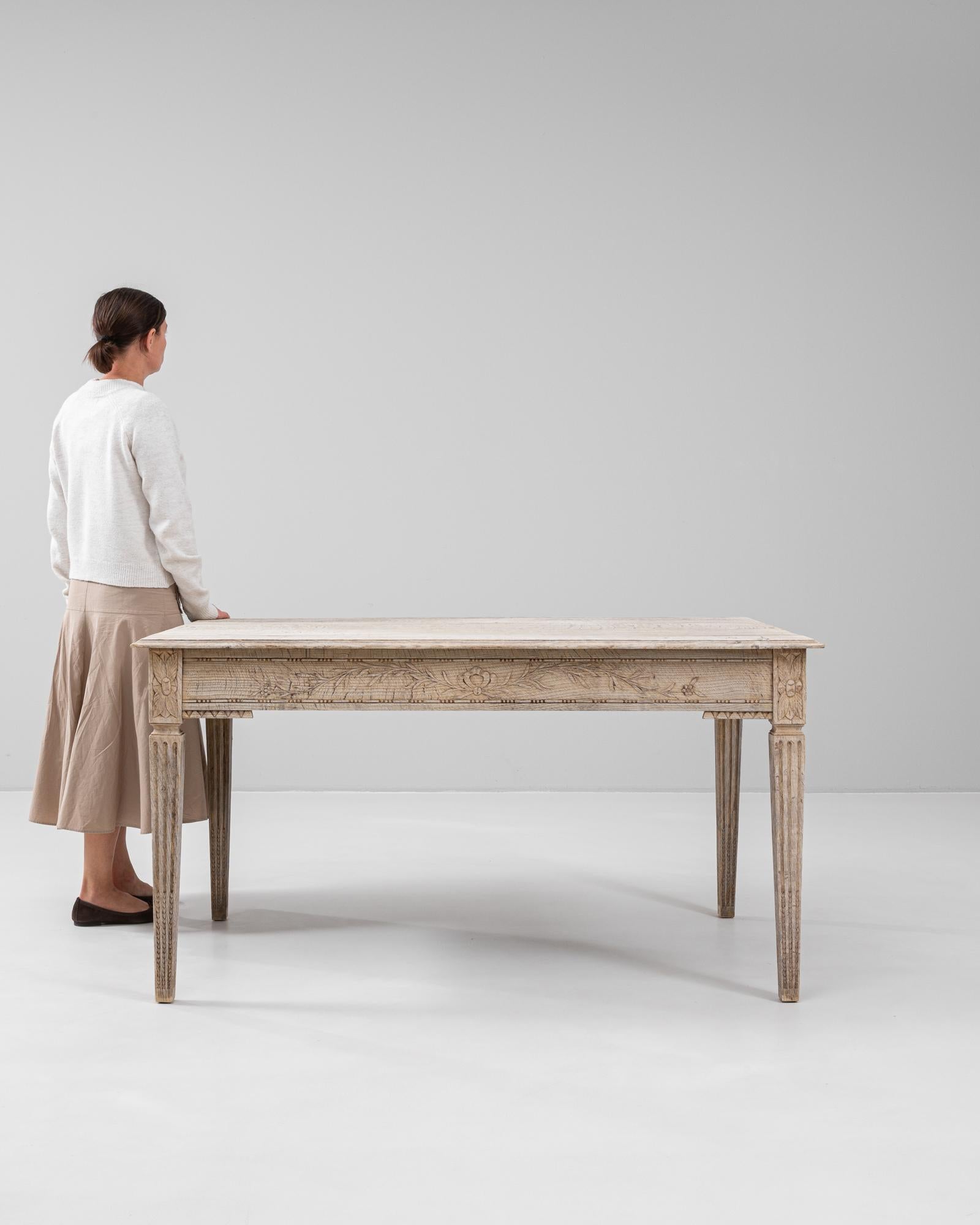 This 19th century French oak dining table captures the elegance of the Louis XVI style with its refined silhouette and delicately carved details. Crafted from solid oak and lightly bleached to reveal its natural grain, the table rests on fluted,